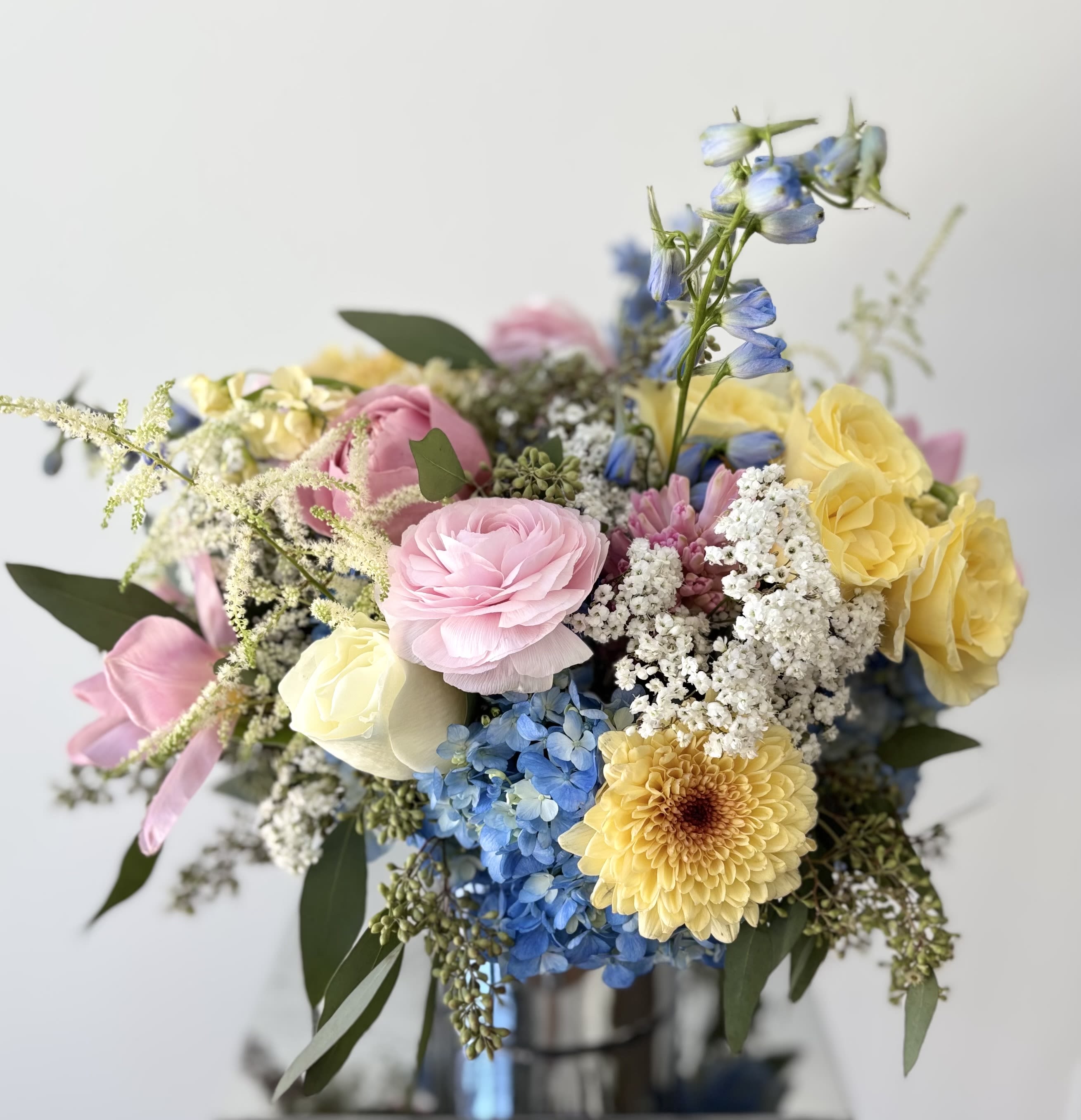 Floriana - A lovely flower arrangement in soft spring colors designed with blue hydrangeas that nestles light pinks, creamy yellows, and gardeny white blooms. Selection of premium flowers may vary based on the availability, usually roses, ranunculus, delphinium, astible, tulips, hyacints and cremons, or simliar.