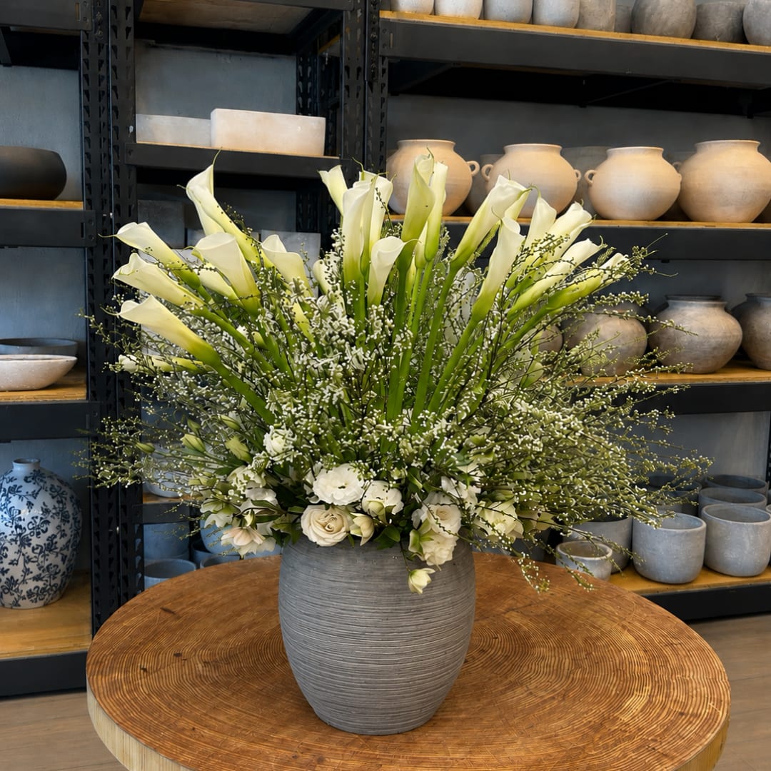 White calla lilies and roses arranged in a gray vase