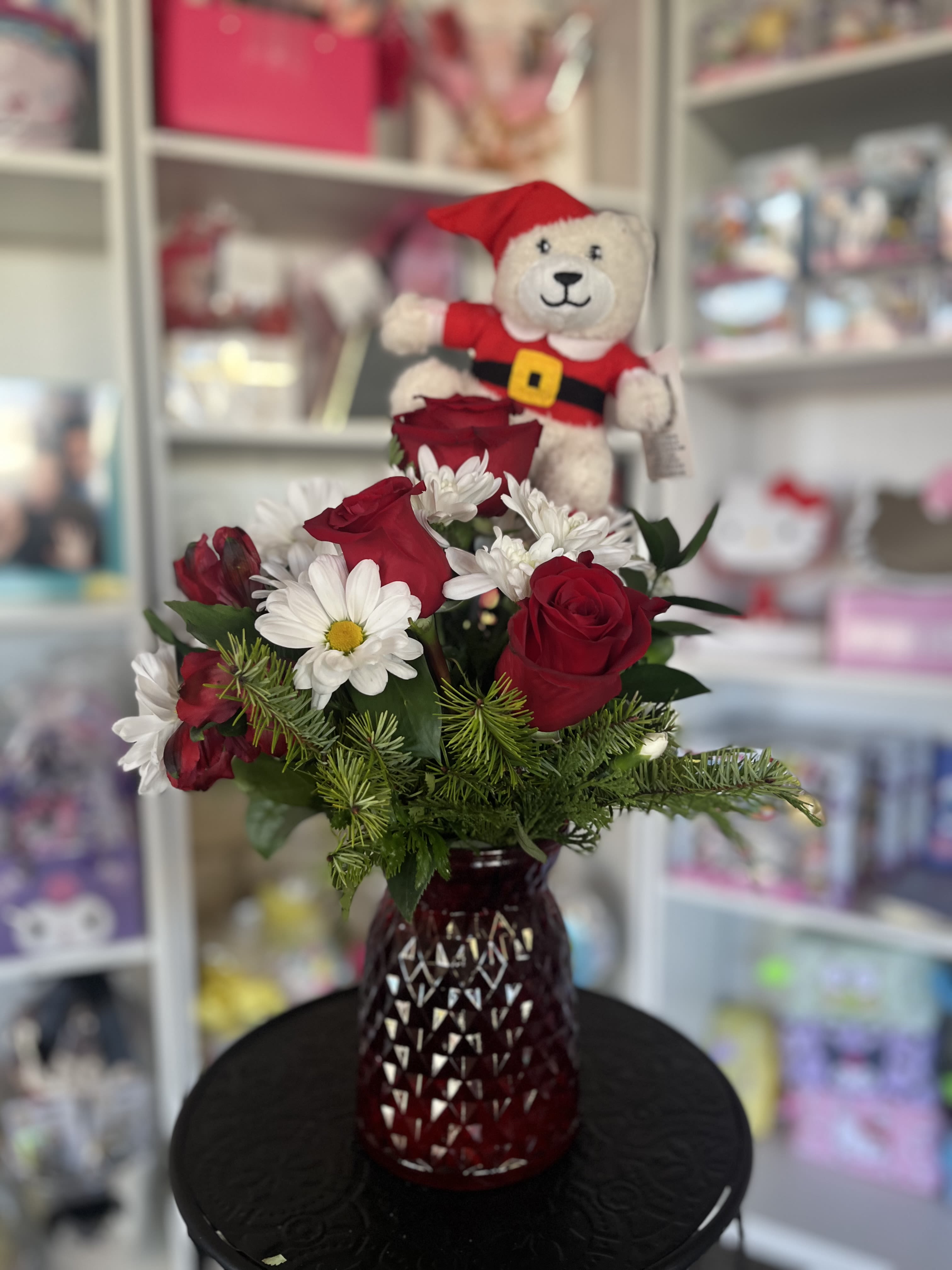 Red roses and white daisies in a red vase with a teddy bear topper