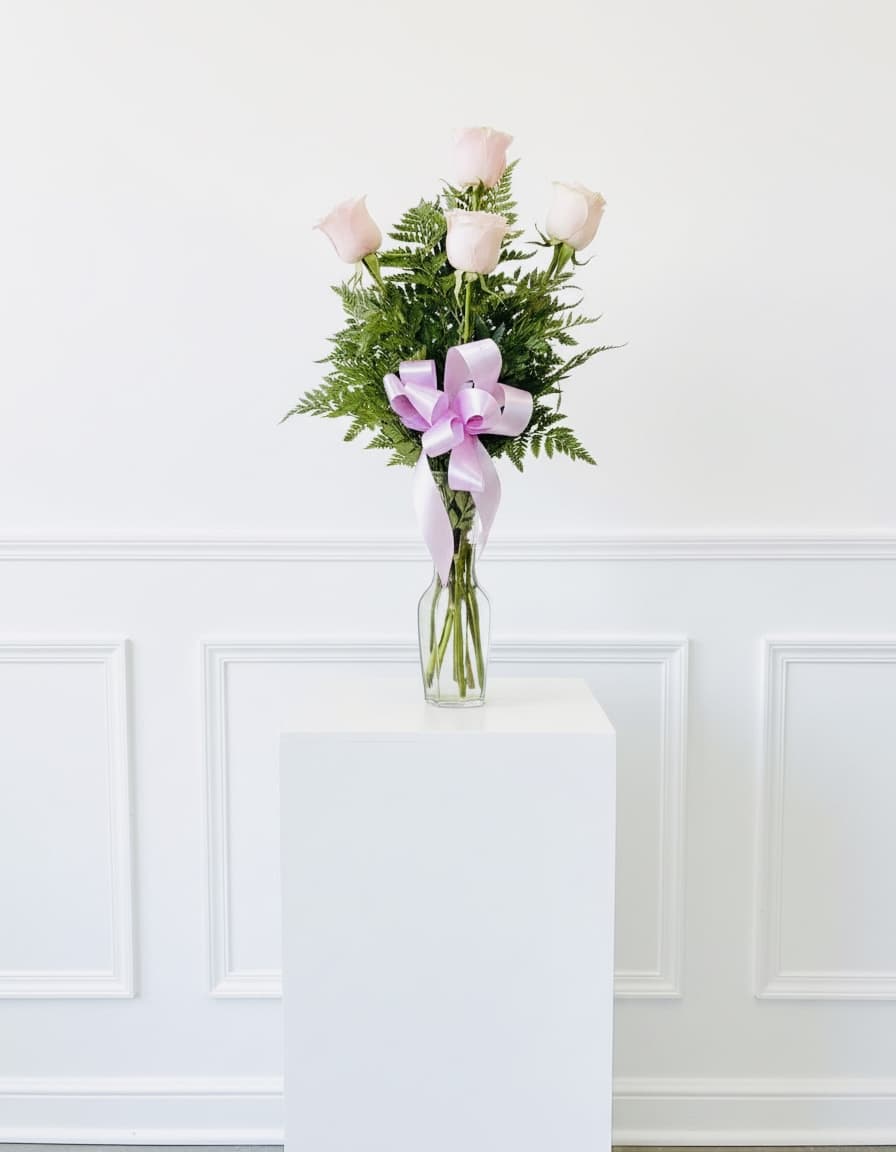 Five pale pink roses in a clear glass vase with a lavender ribbon