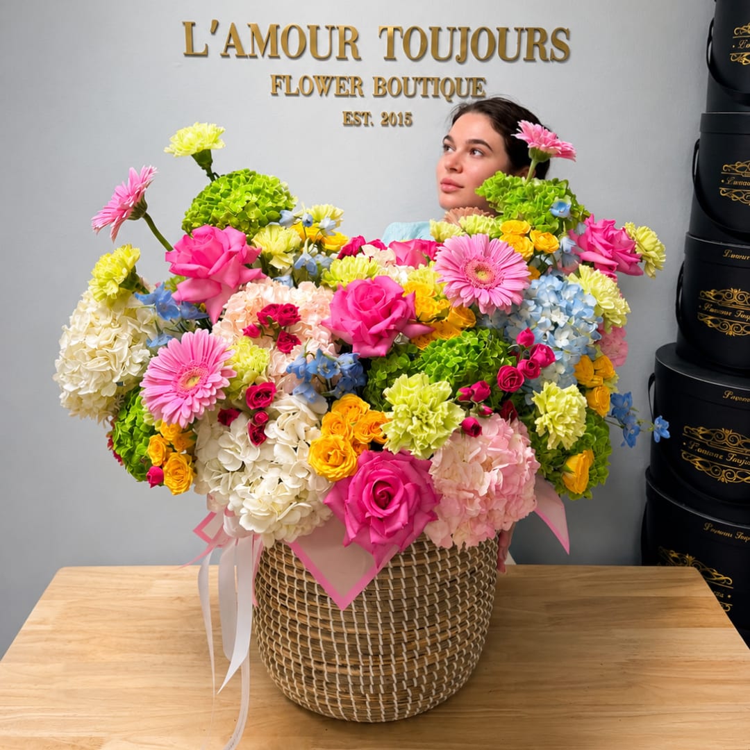 Large mixed flower arrangement in a woven basket with pink and yellow blooms