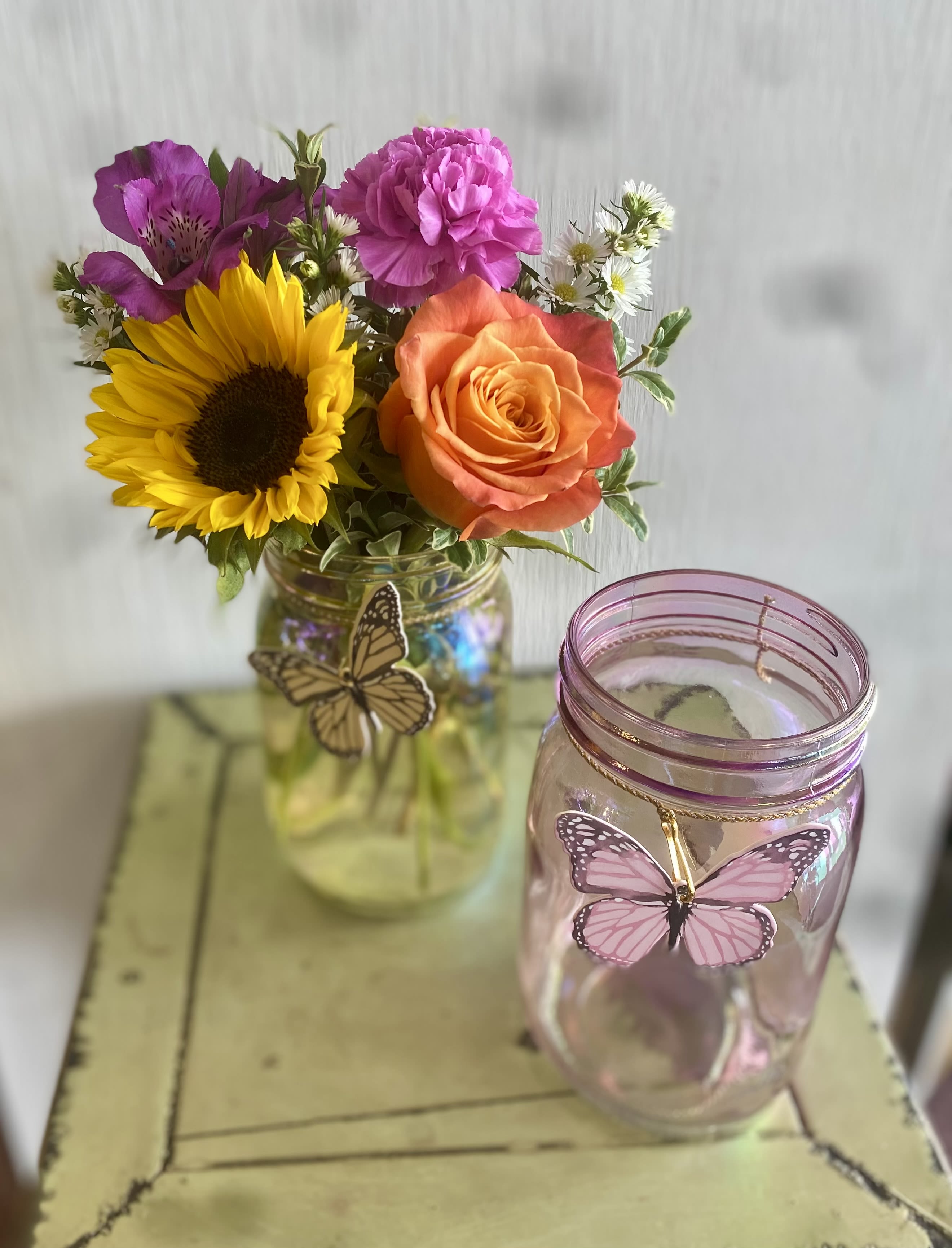 Mixed bouquet in a glass jar beside a pink butterfly jar candle
