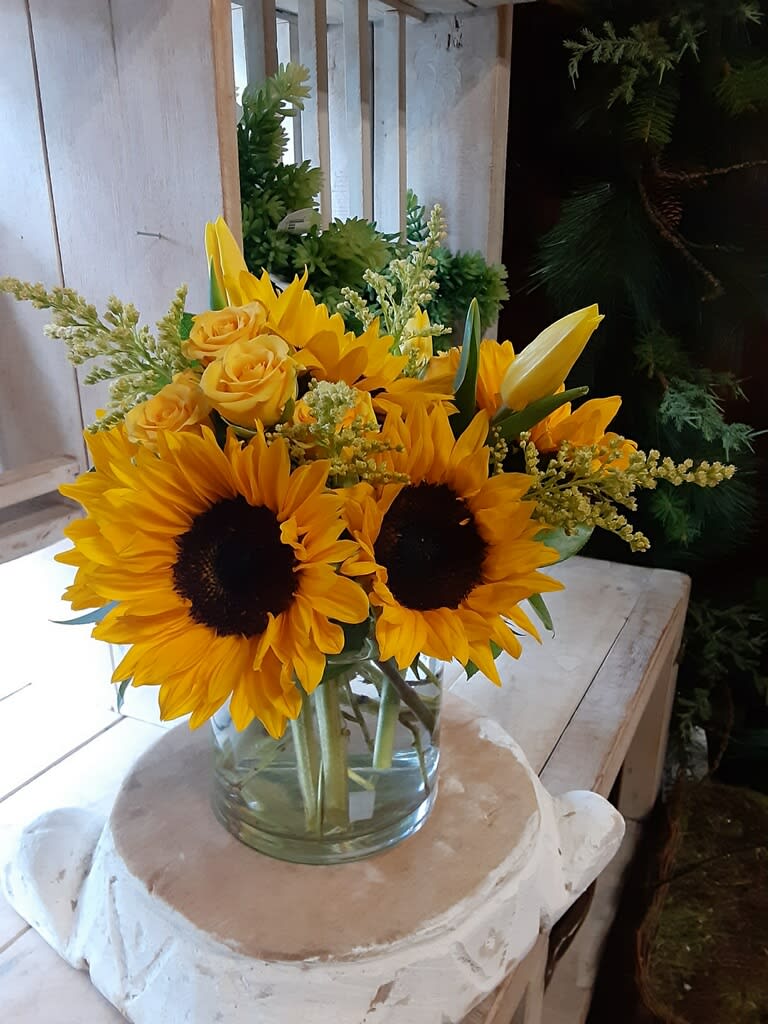 Sunflowers and yellow roses arranged in a clear glass vase