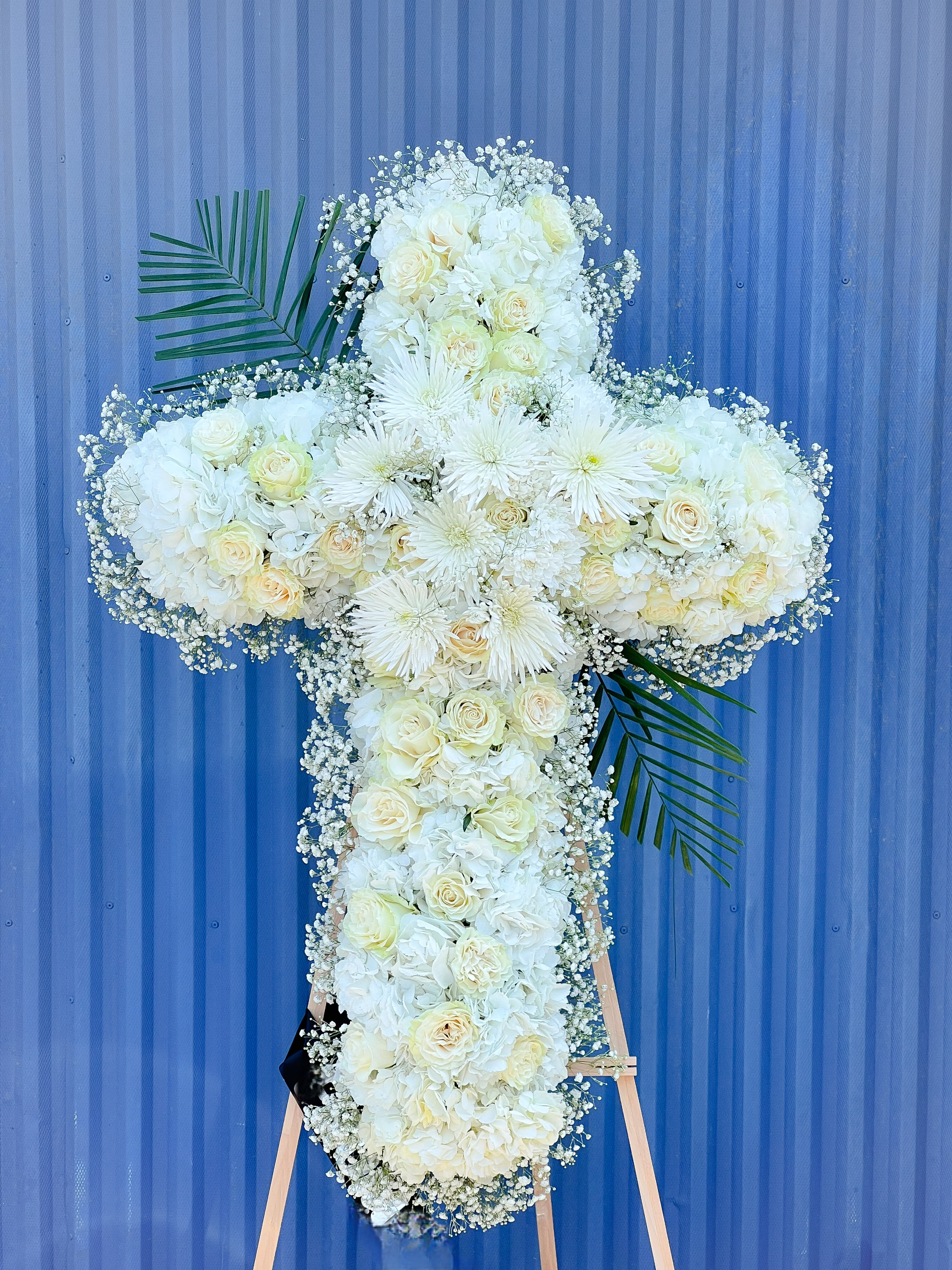 White floral cross arrangement on an easel with palm fronds