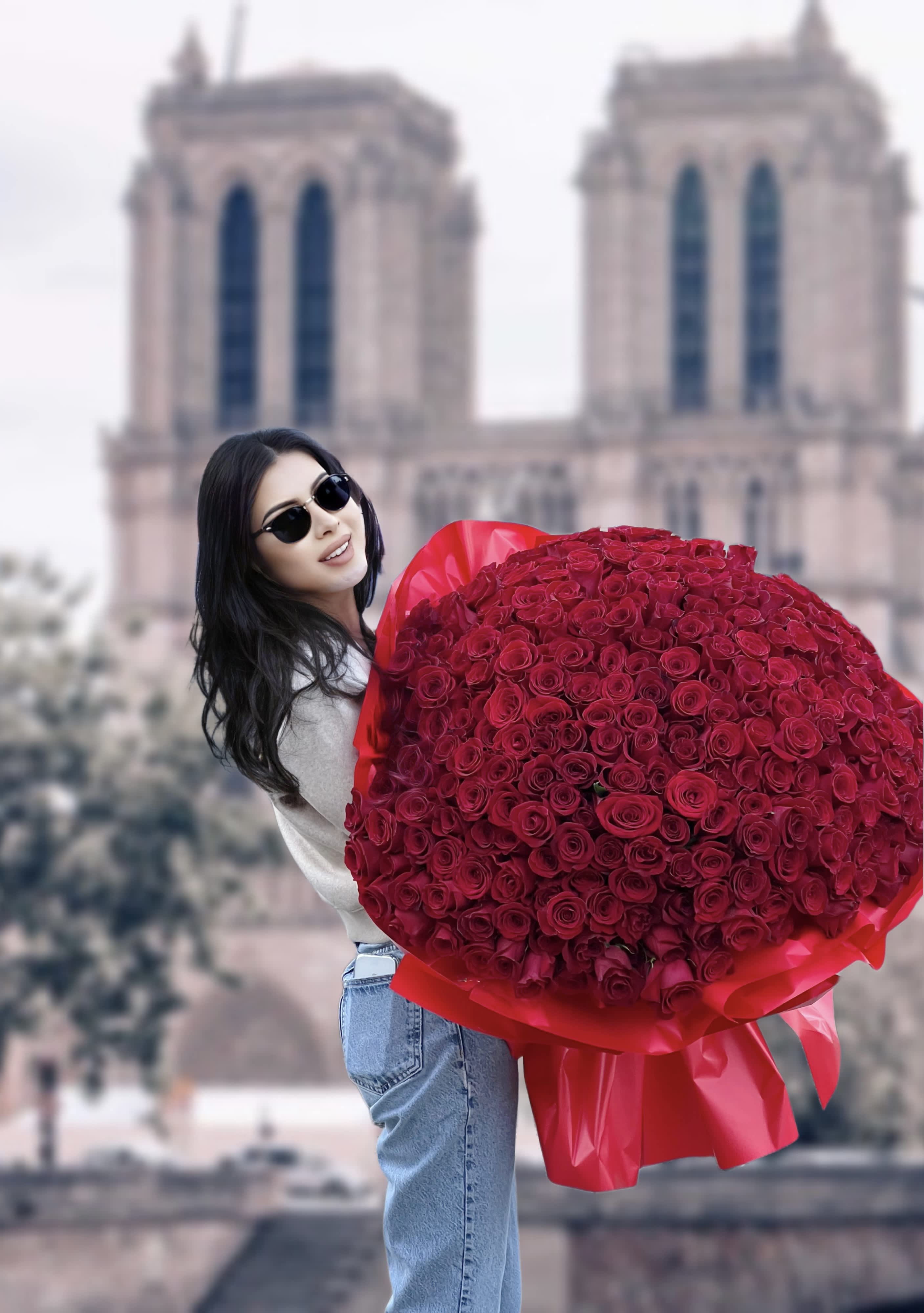 Woman holding a large bouquet of red roses in front of a cathedral