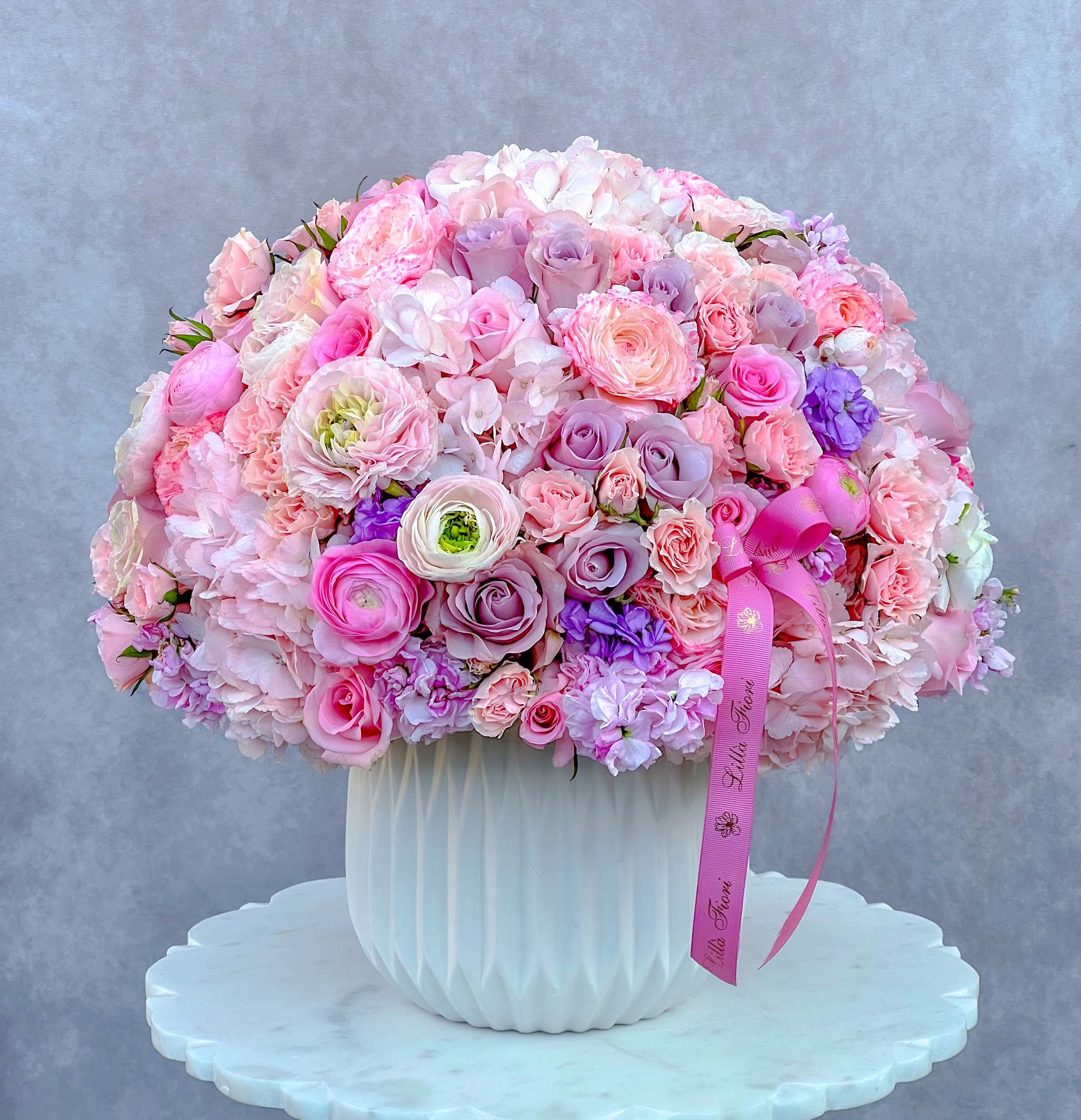 Large pink and lavender bouquet in a white vase with a ribbon