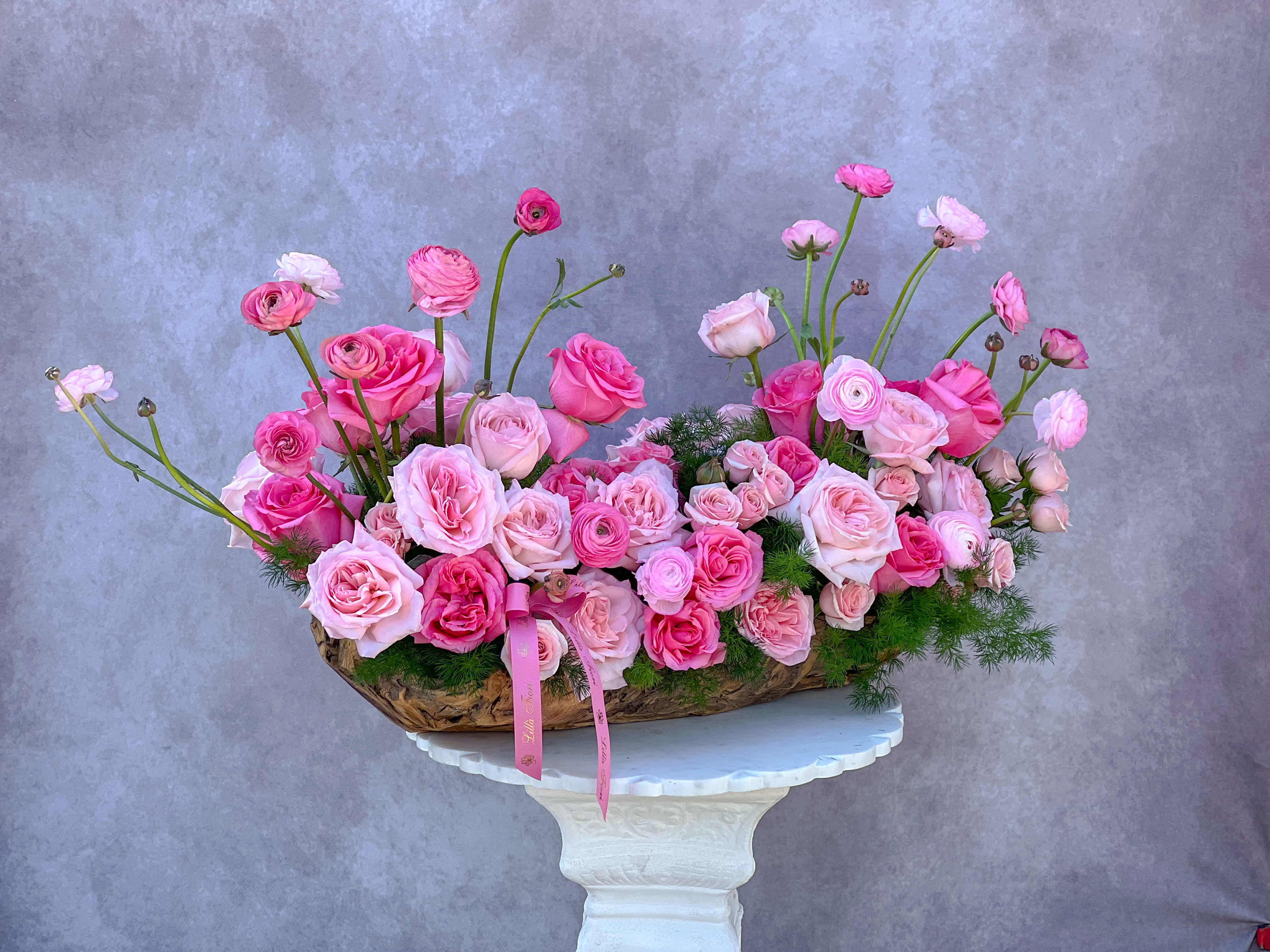 Pink roses and ranunculus arranged in a low basket on a pedestal