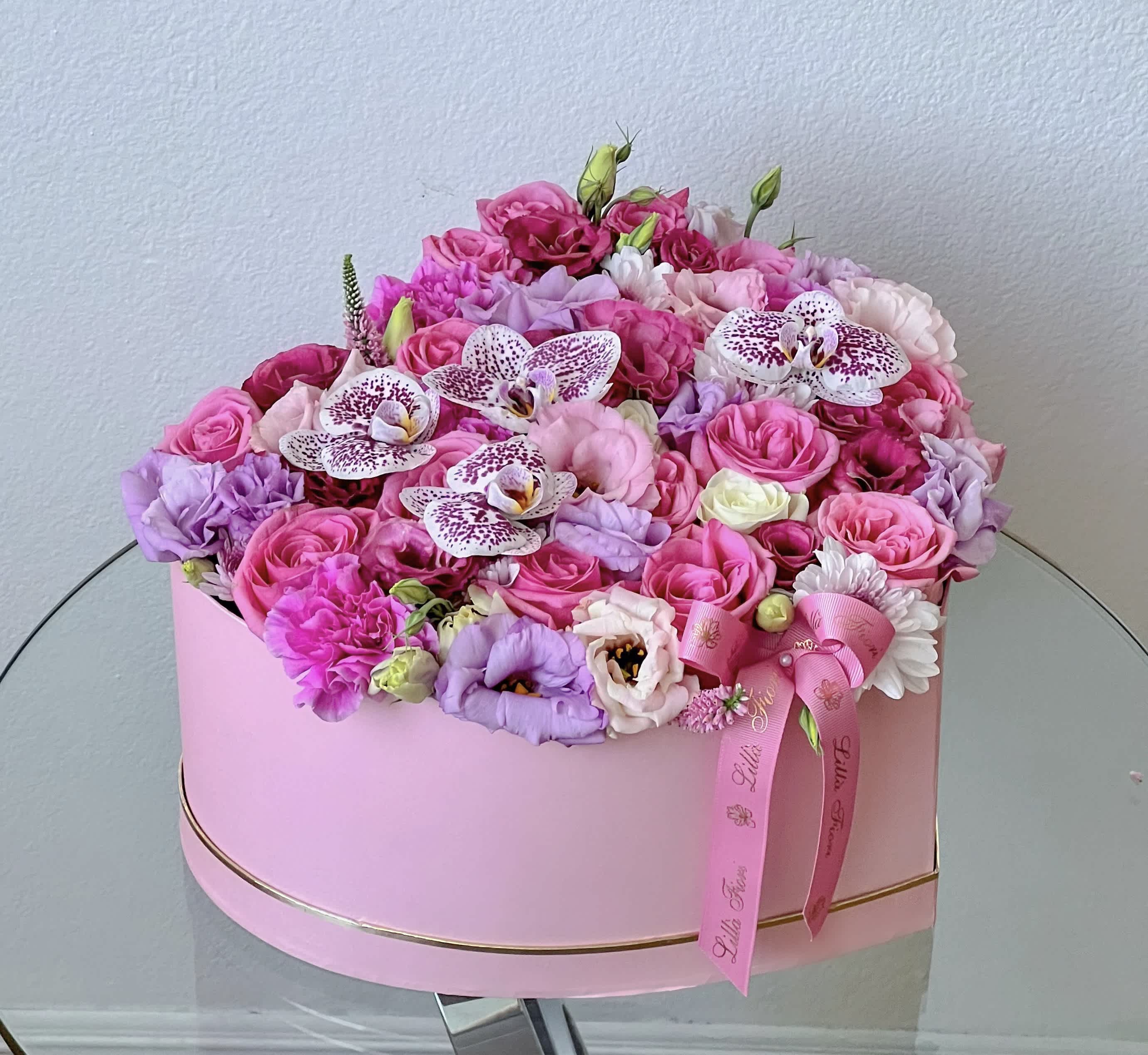 Pink and lavender floral arrangement in a round pink box with ribbon