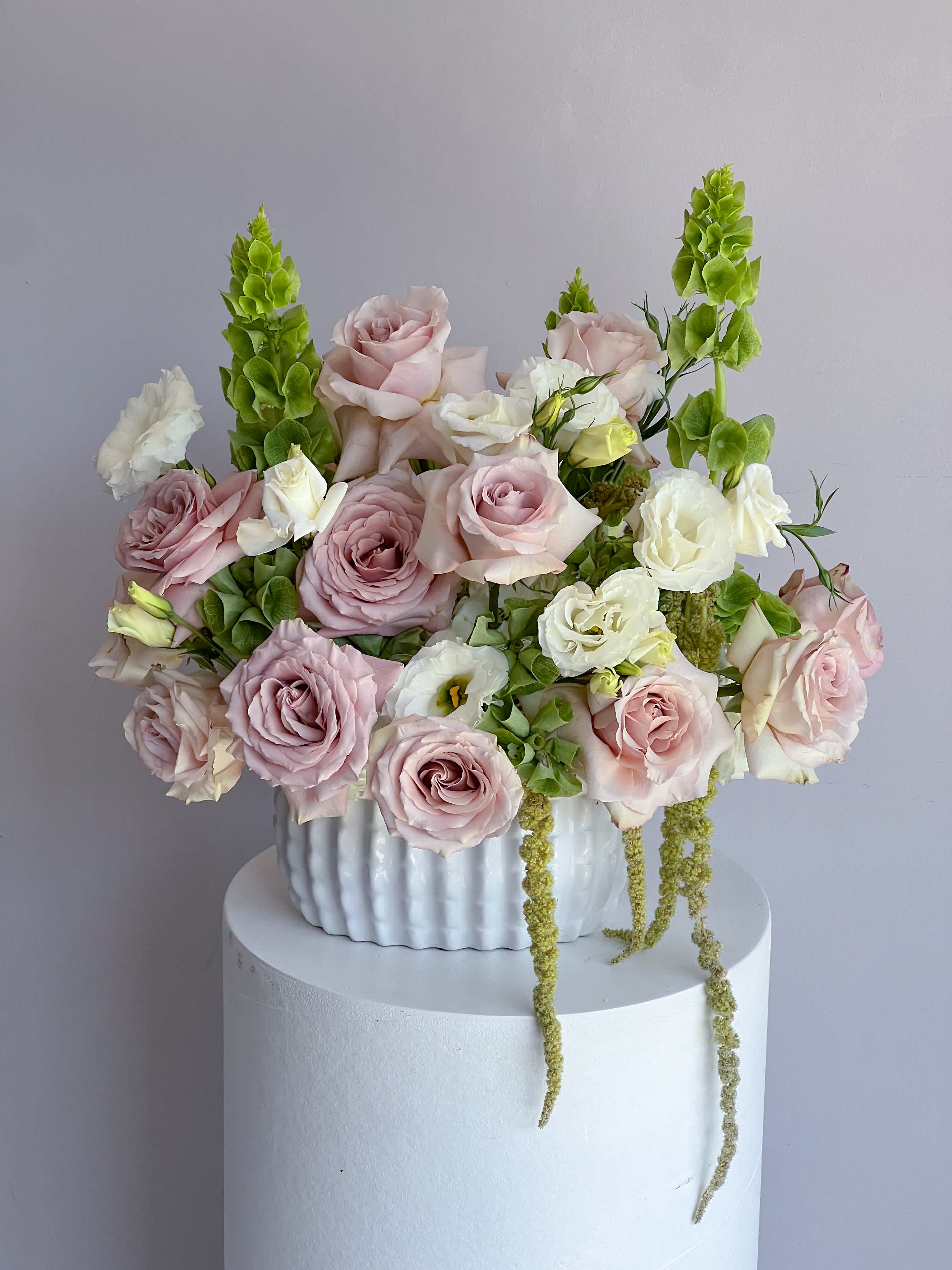 Pink and white roses arranged in a white vase with green spikes