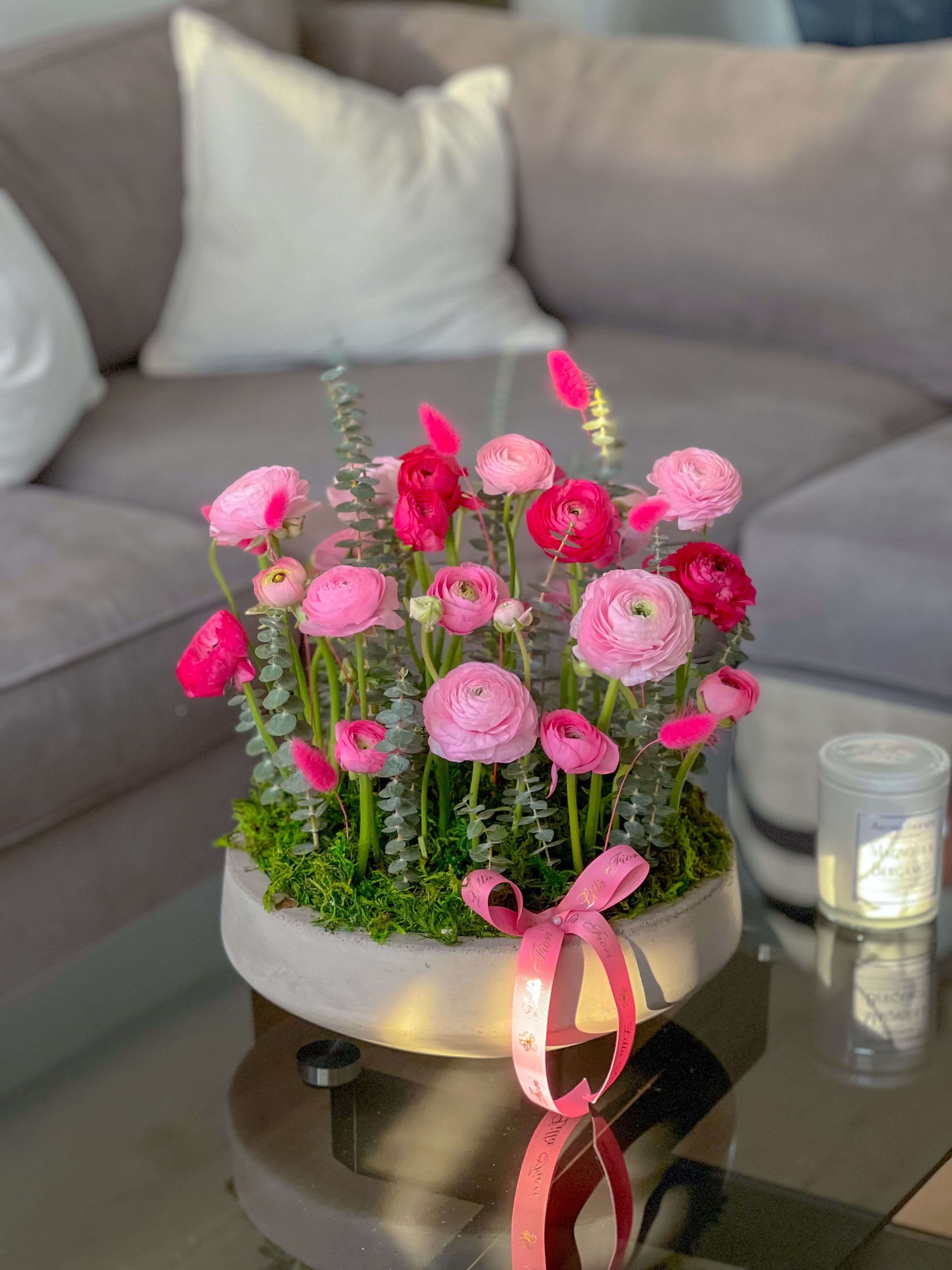 Pink ranunculus arrangement in a round white container with a ribbon