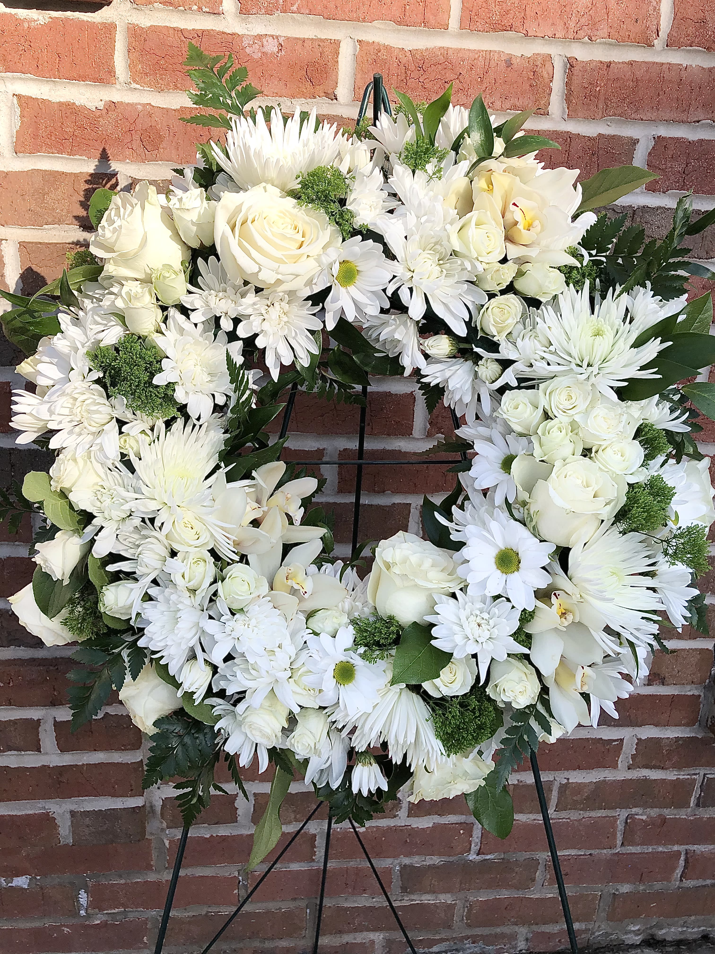 White floral wreath on a black stand with roses and daisies
