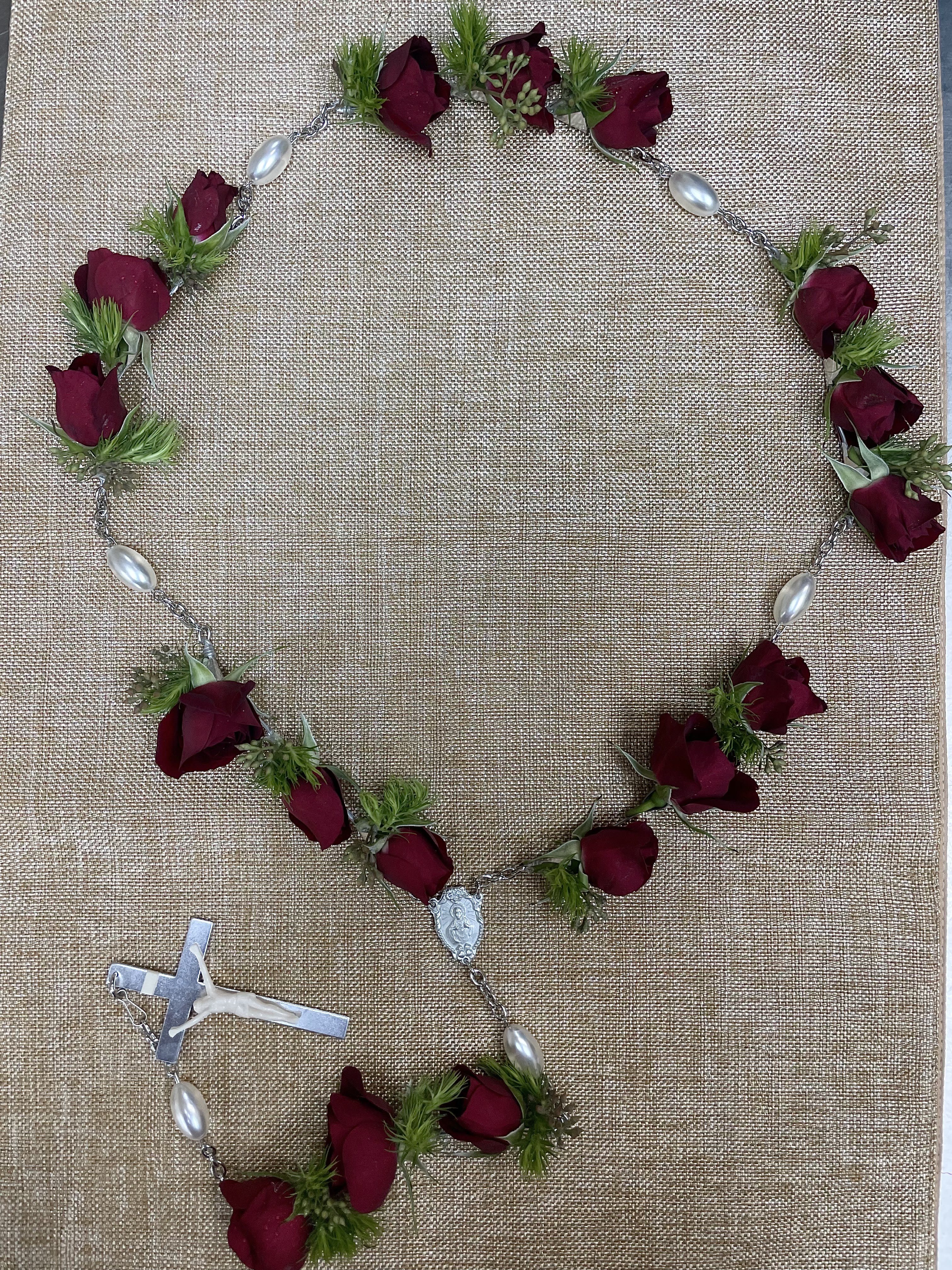 Rose petal rosary with silver beads and a crucifix on burlap
