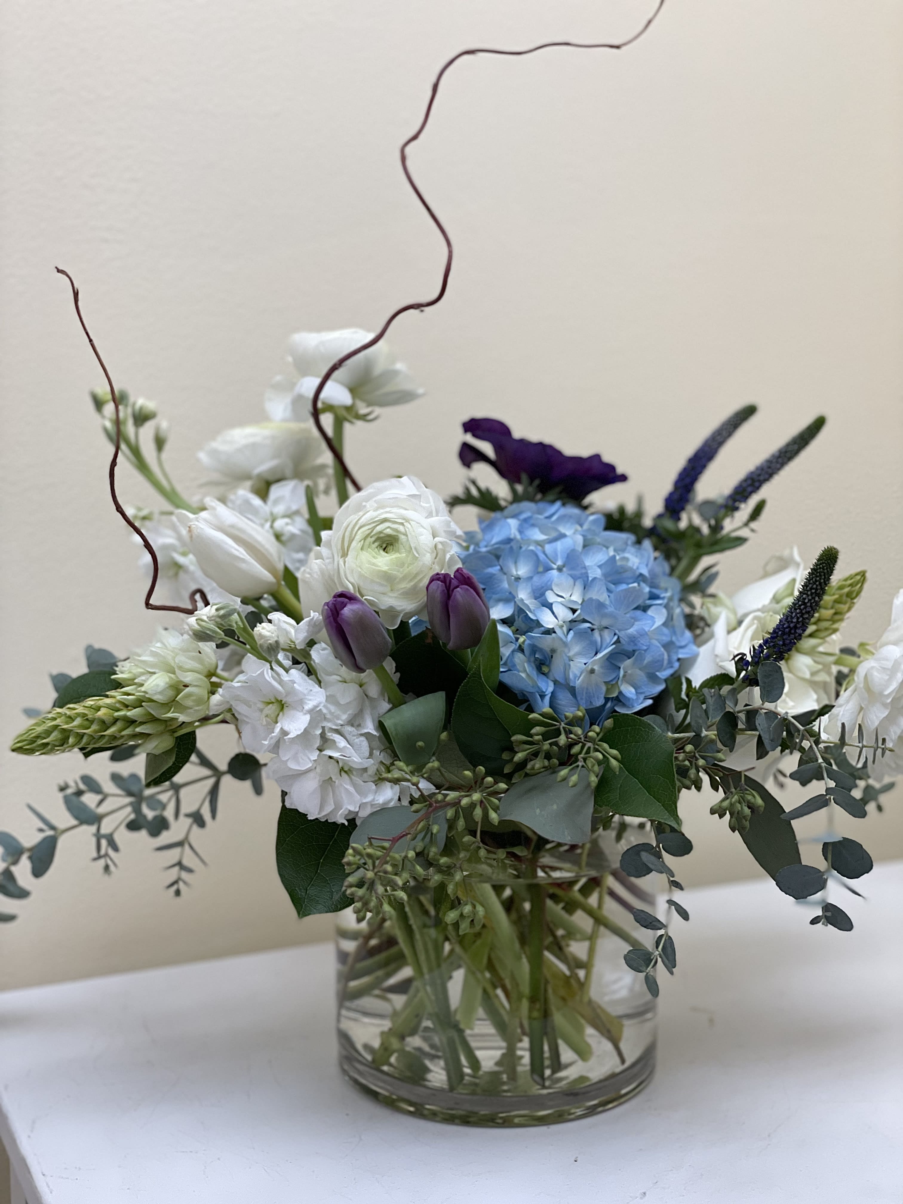 Mixed bouquet in a clear glass vase with blue hydrangea, white blooms, and purple tulips