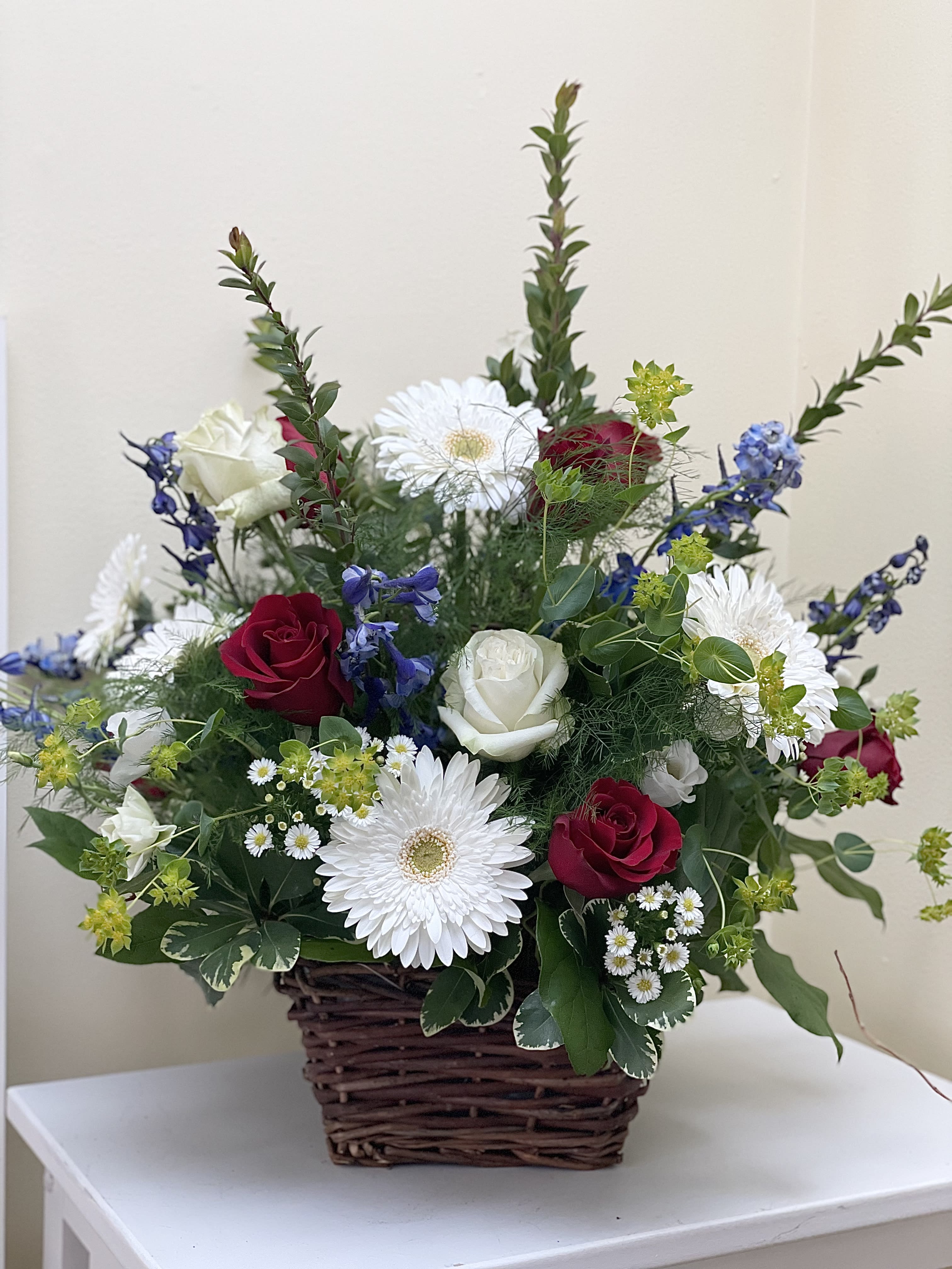 Basket arrangement with red and white roses, white daisies, and blue flowers