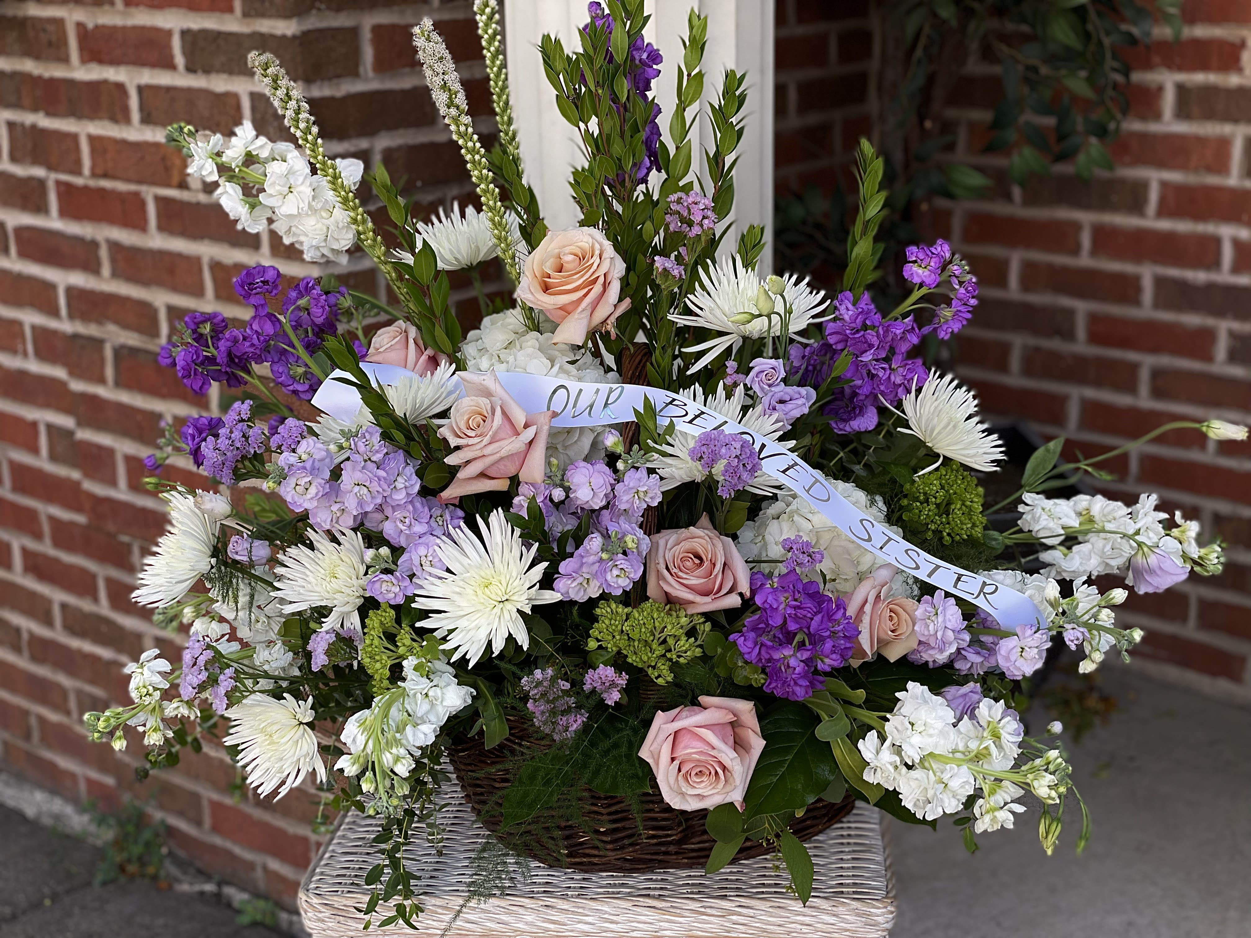 Basket arrangement of pink roses, white daisies, and purple flowers with a ribbon