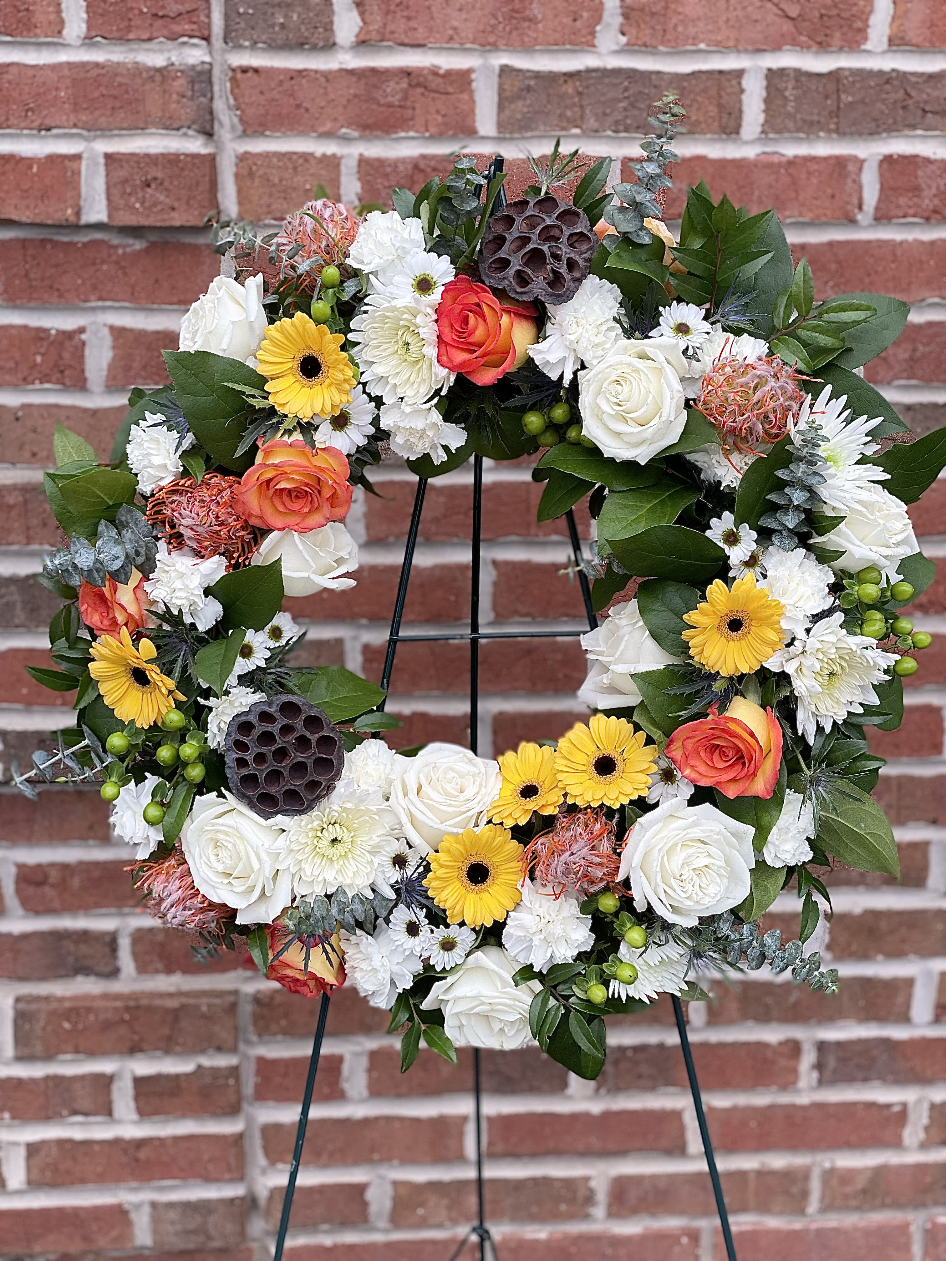Floral wreath with white, yellow, and orange blooms on a black stand