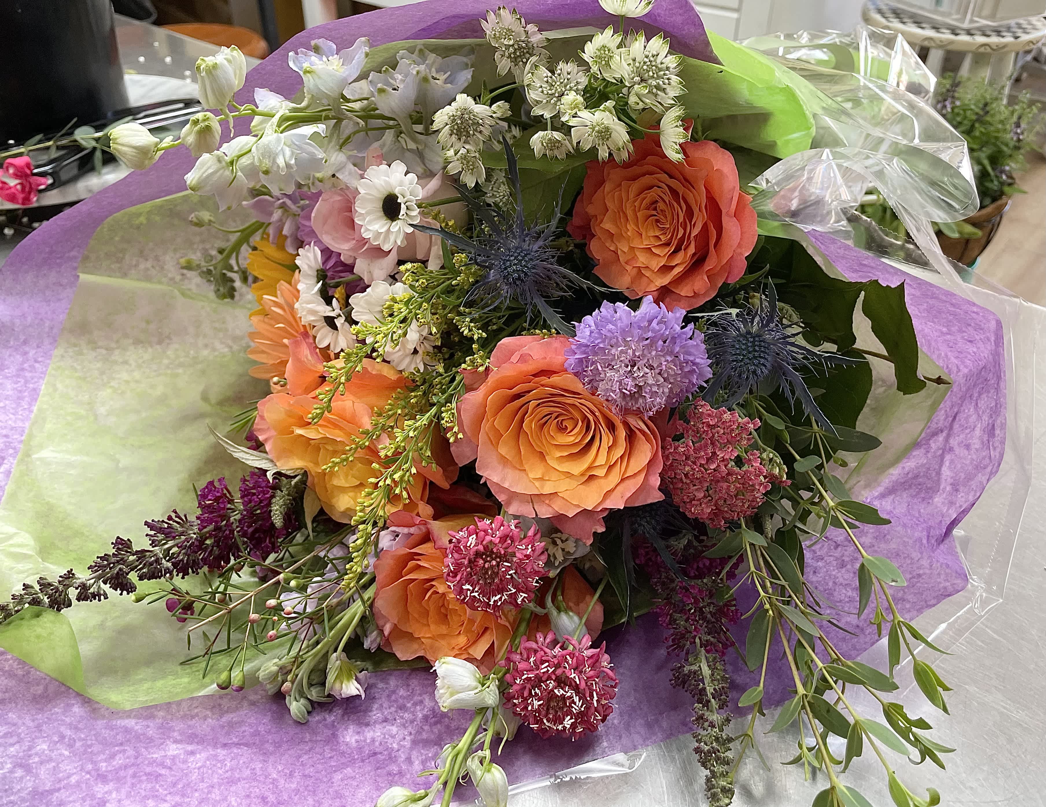 Mixed bouquet with orange roses and purple flowers wrapped in purple paper