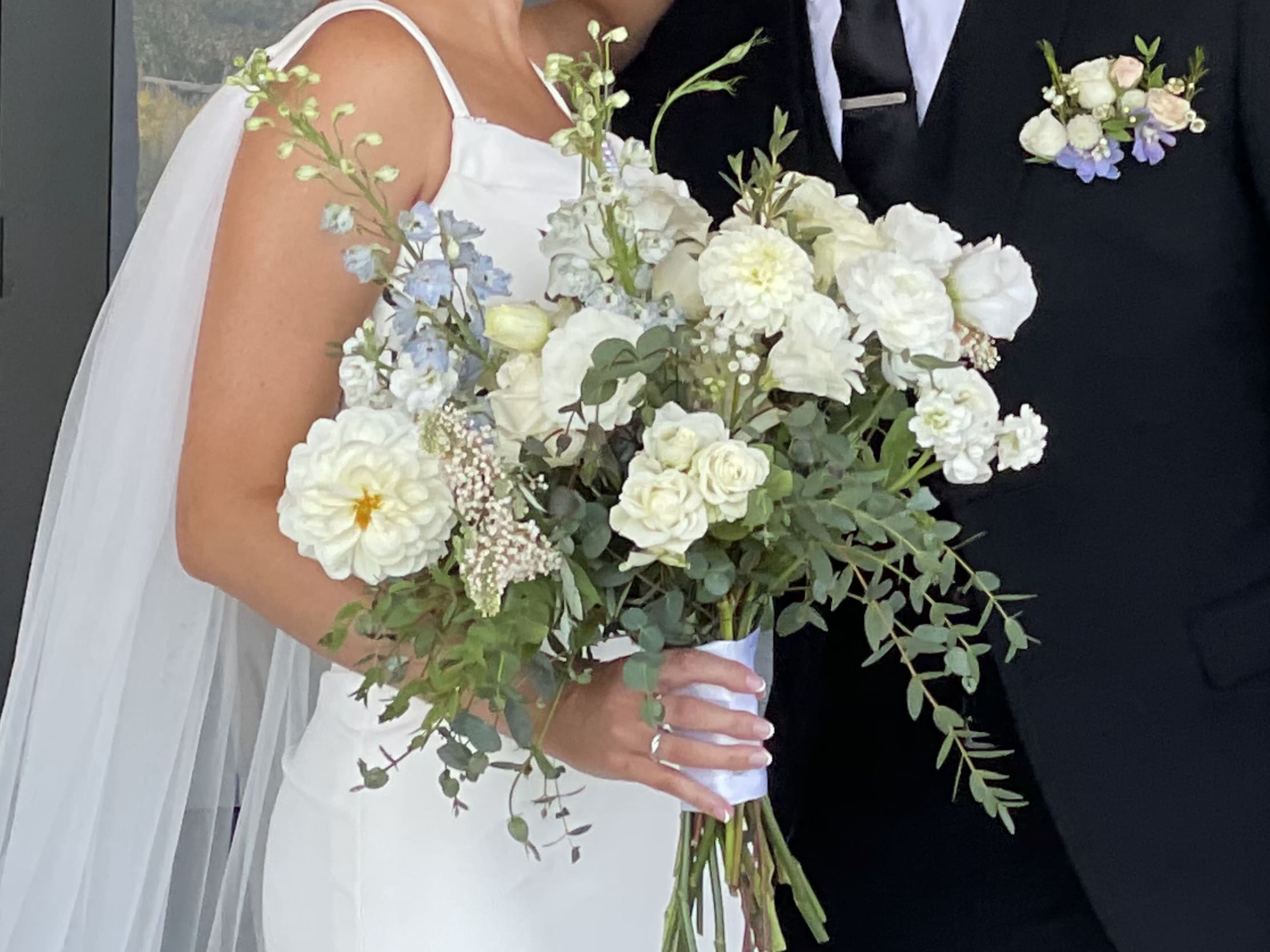 Bride holding a white and pale blue bouquet beside a groom in a black suit