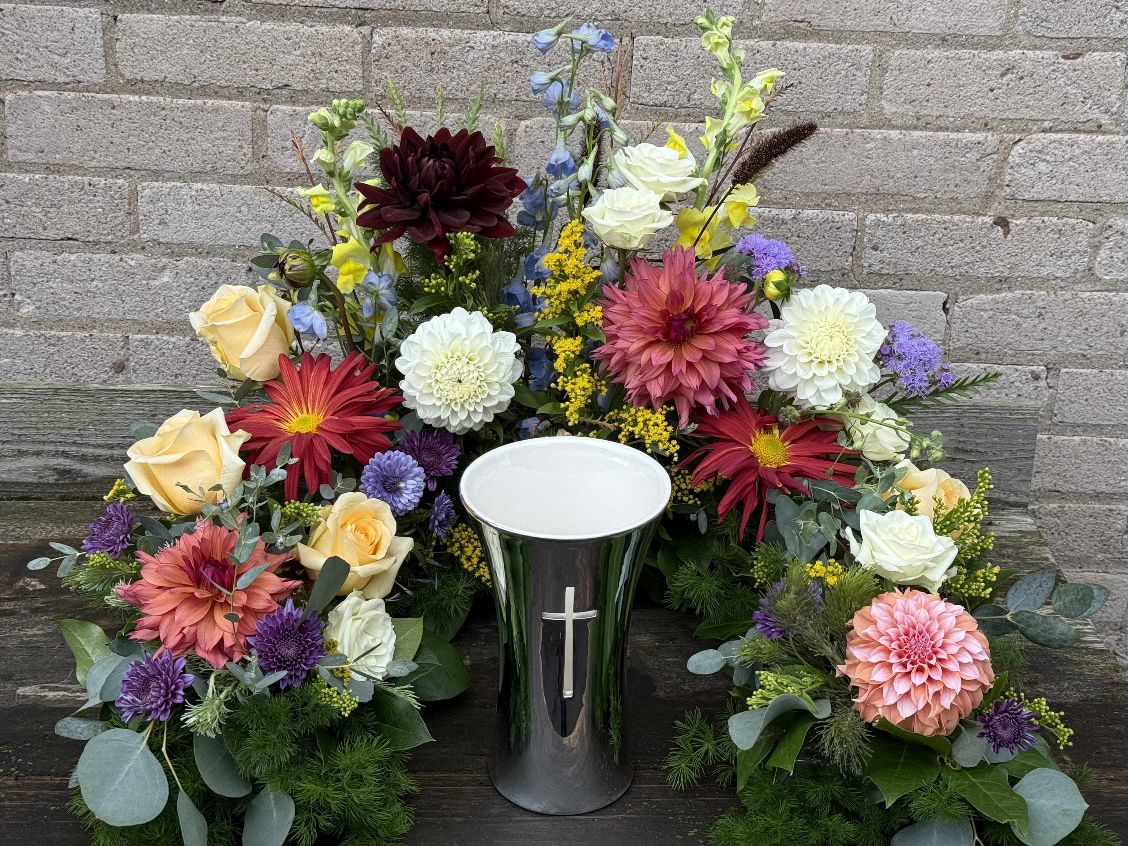 Colorful floral arrangement around a black urn with a cross
