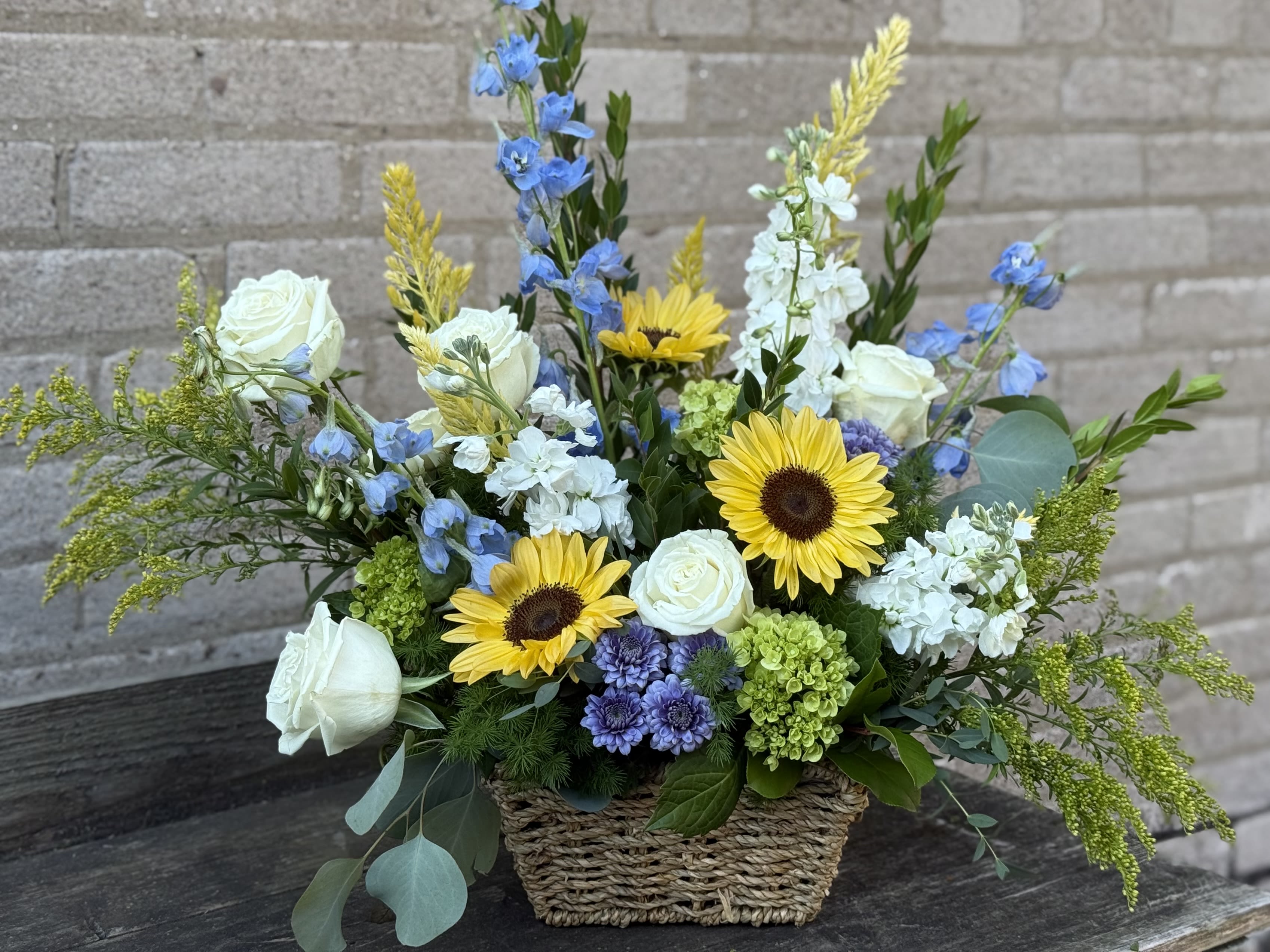 Basket arrangement with white roses, sunflowers, and blue flowers