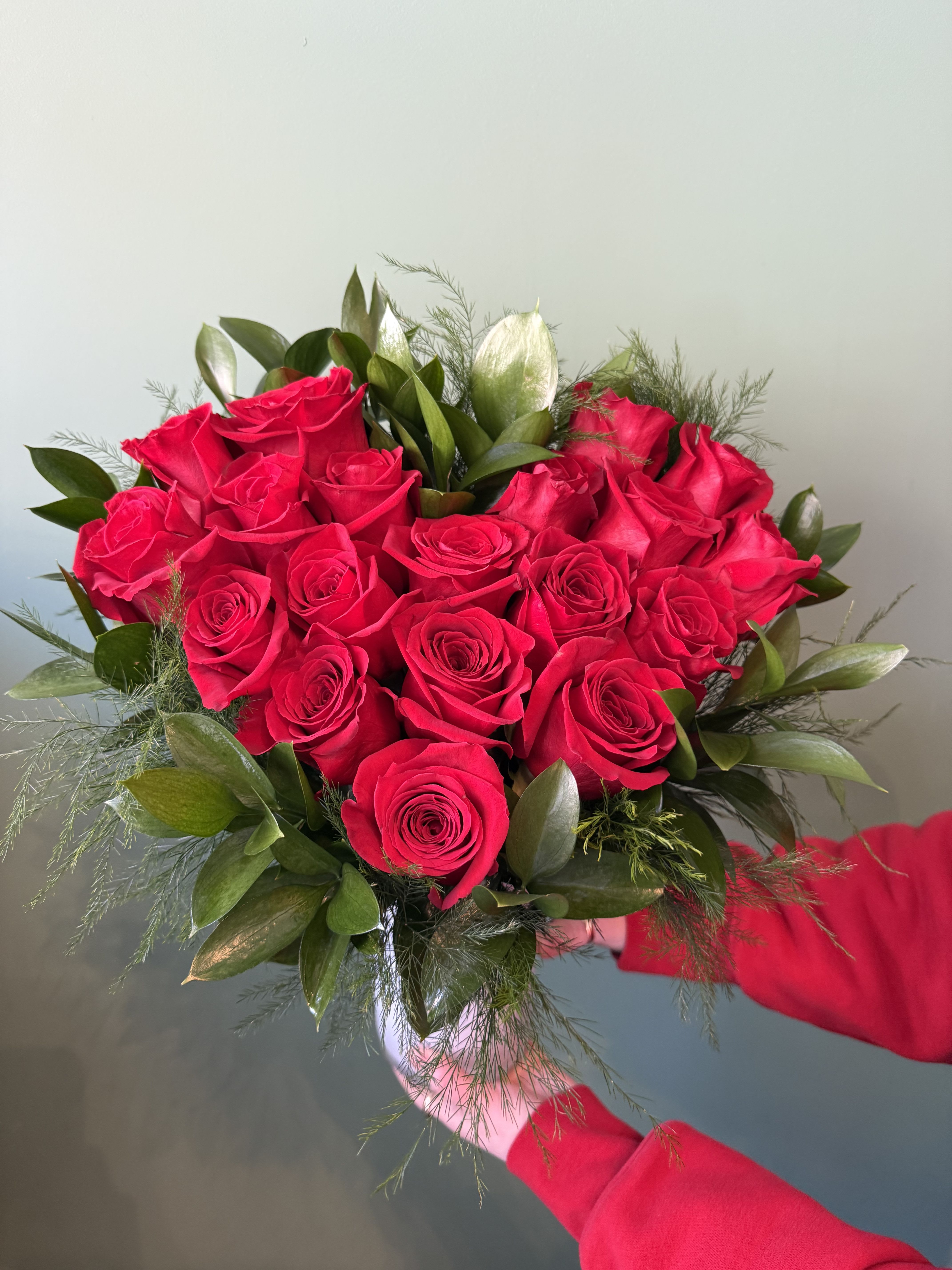 Handheld bouquet of red roses with green foliage