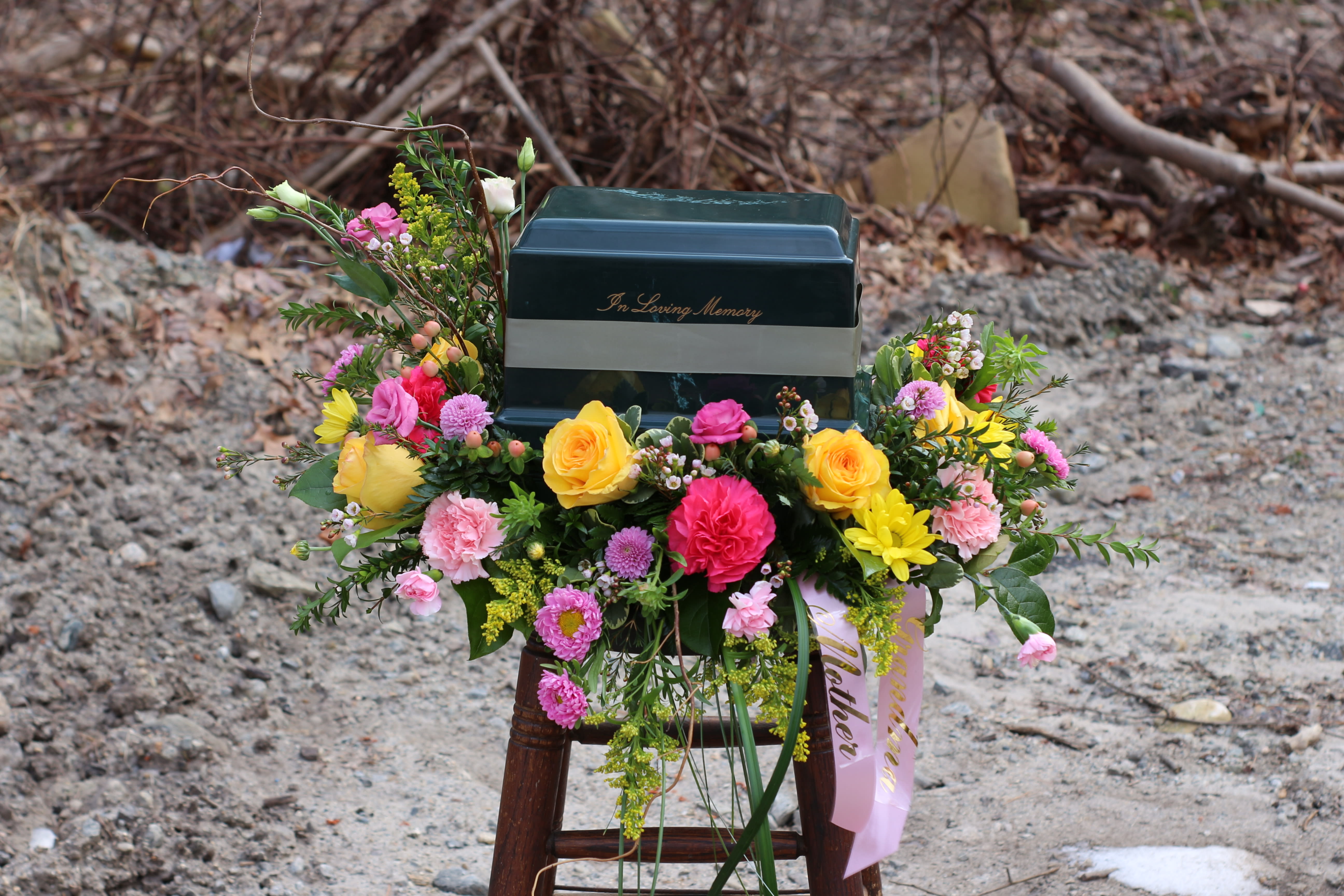 Colorful funeral spray around a dark urn with "In Loving Memory" text