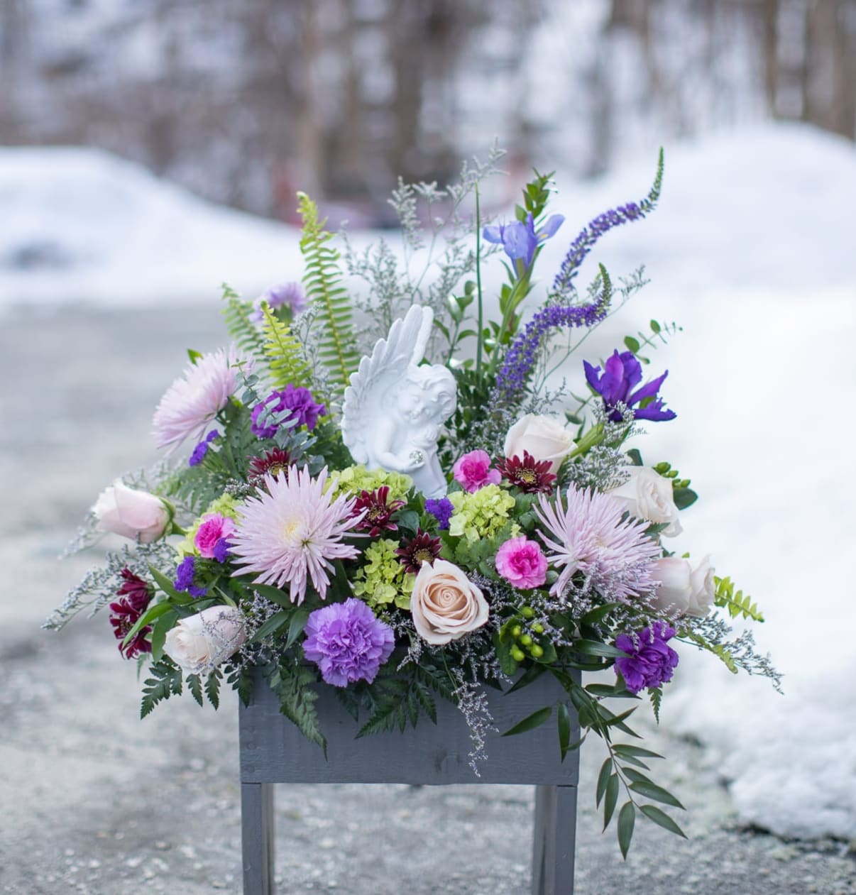 Purple and white floral arrangement in a gray container with an angel figurine