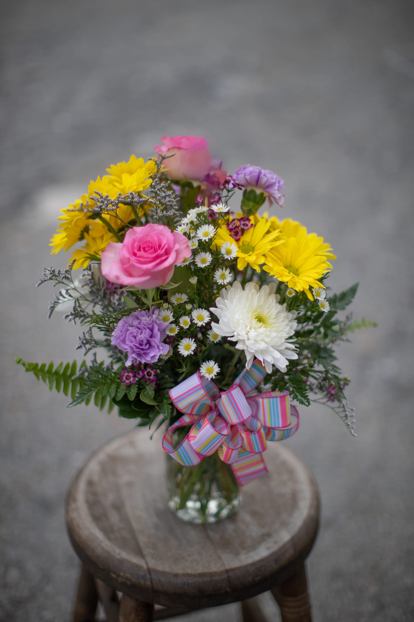 Mixed bouquet of pink, yellow, white, and purple flowers in a glass vase