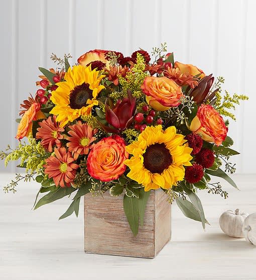 Harvest Glow Bouquet - The color and charm of an autumn country harvest inspired our new farmhouse-style bouquet. A loose, natural gathering of blooms in vibrant shades of red, orange and yellow creates the perfect complement to our rustic, grey washed wooden cube. With its soft tones and natural textures, it’s an ideal container for flowers and plants, adding warm and coziness to any fall décor. •All-around arrangement with red button poms, leucadendron and hypericum, autum-colored roses, sunflowers, bronze daisy poms; accented with solidago and assorted greenery •Artistically designed in our exclusive grey washed wooden cube with rustic style and natural, textural beauty; measures 5.2"L x 5.2"H x 5.2"W 