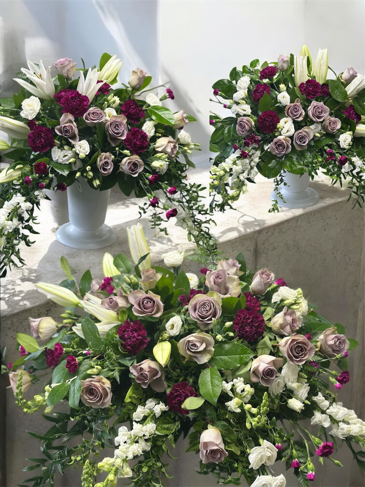 Three floral arrangements in white pedestal vases with roses and lilies