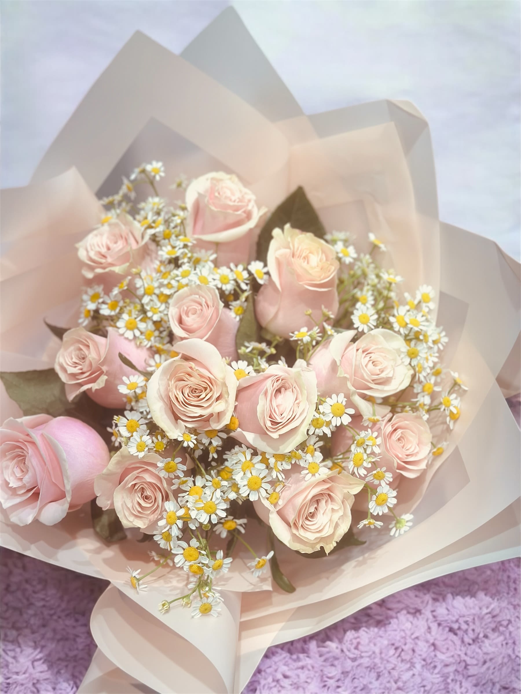 Bouquet of pale pink roses and small white daisies in blush wrapping