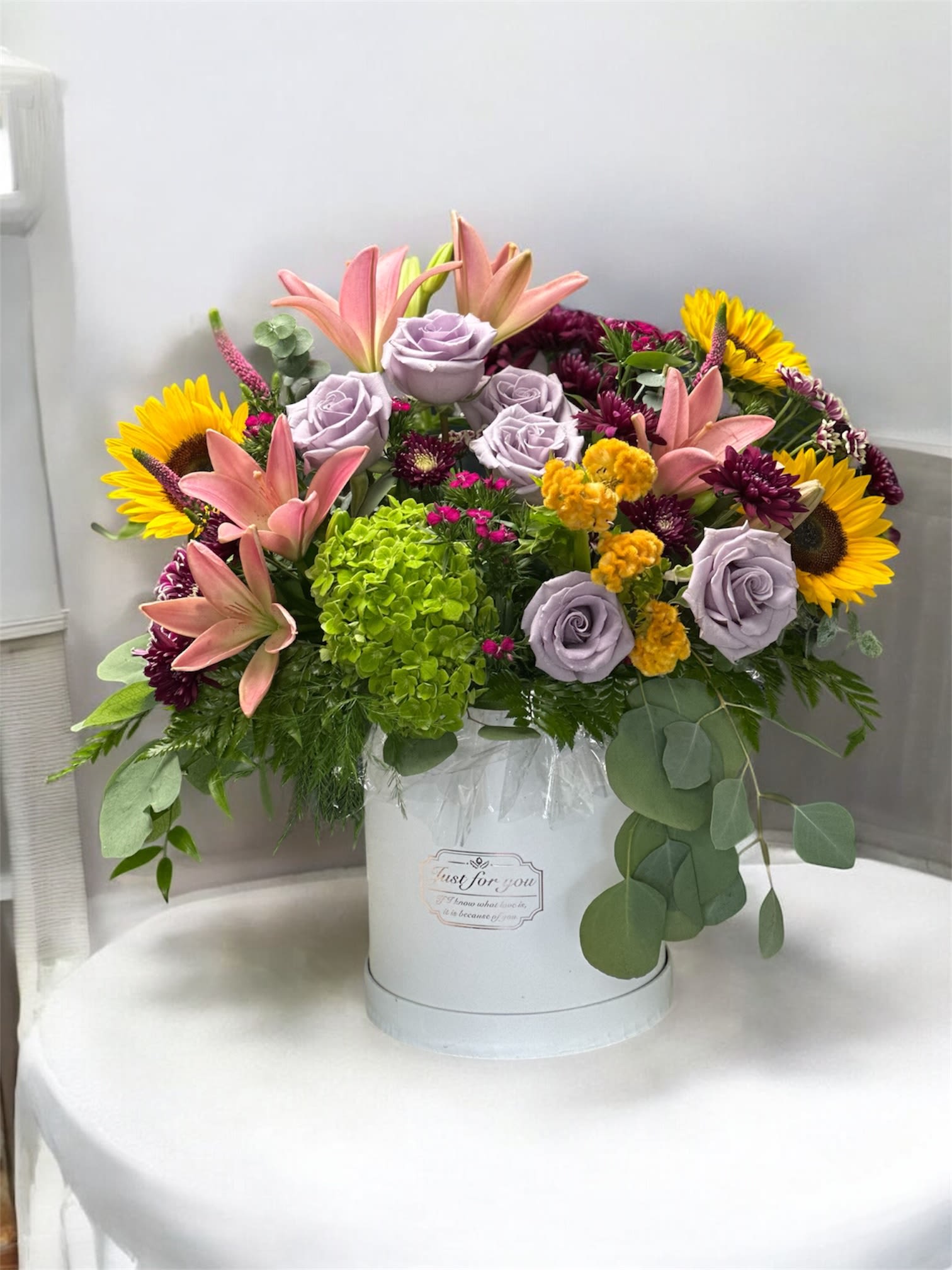 Mixed bouquet in a white hat box with sunflowers, lilies, and lavender roses