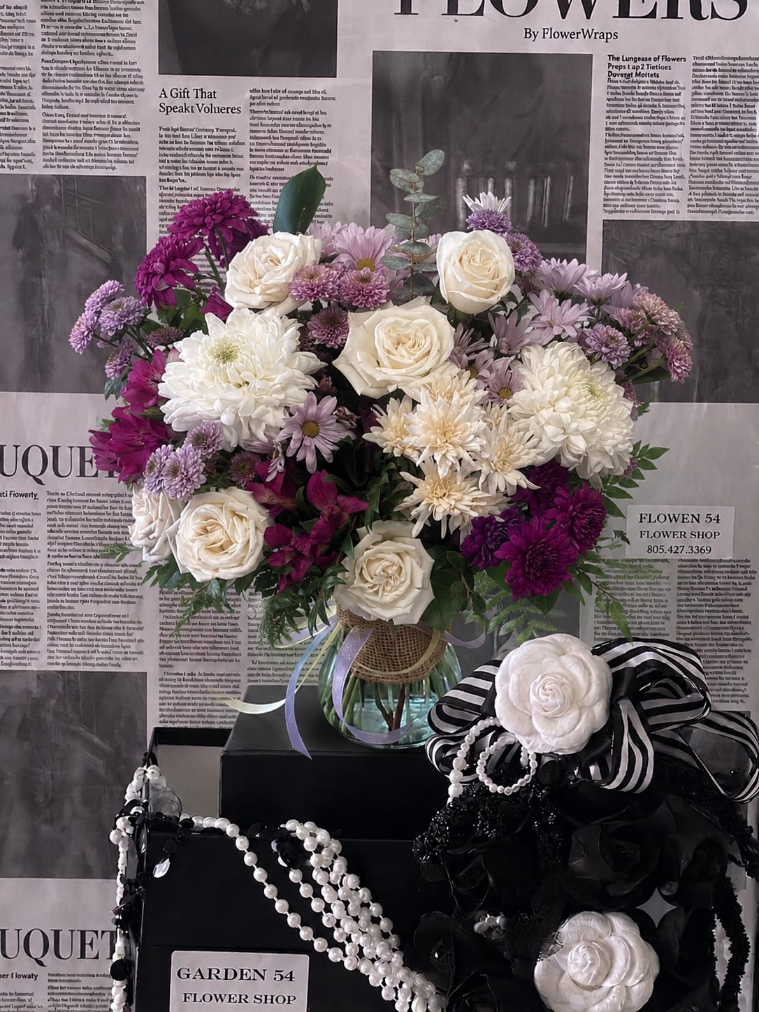 Bouquet of white and purple flowers in a glass vase with black-and-white ribbon accents