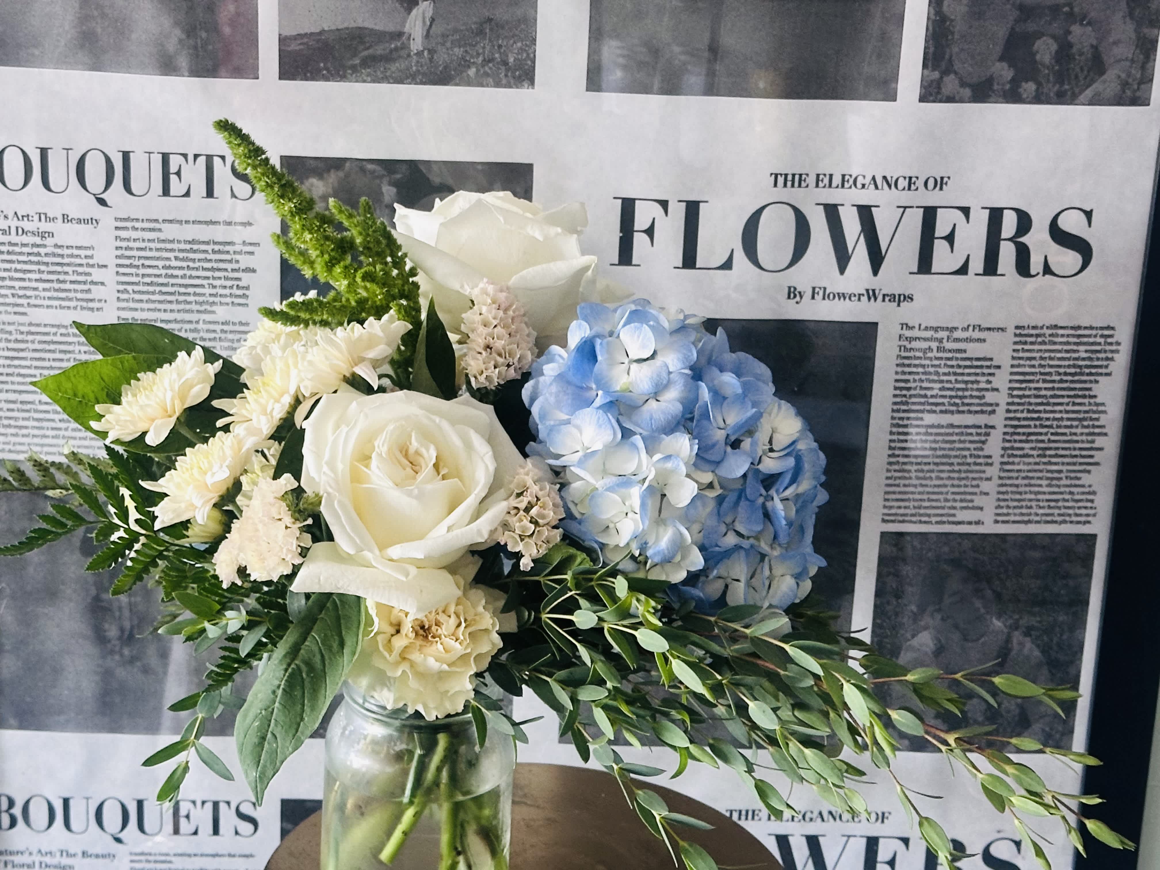 Bouquet of white roses, blue hydrangea, and cream flowers in a glass jar