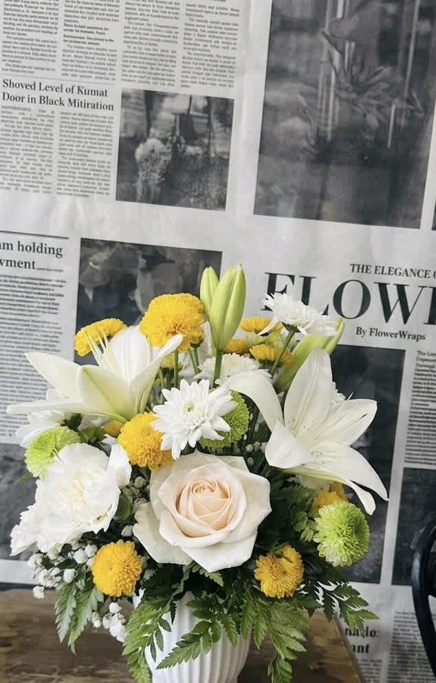 White lilies and yellow pompons arranged in a white vase with a pale rose center