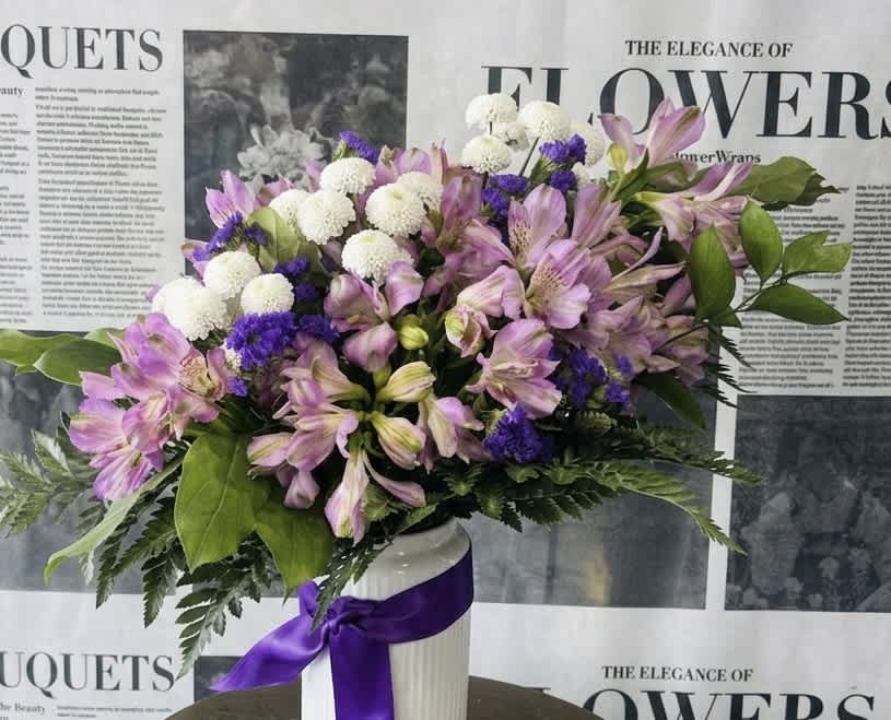 Pink alstroemeria and white pompom flowers in a white vase with a purple ribbon