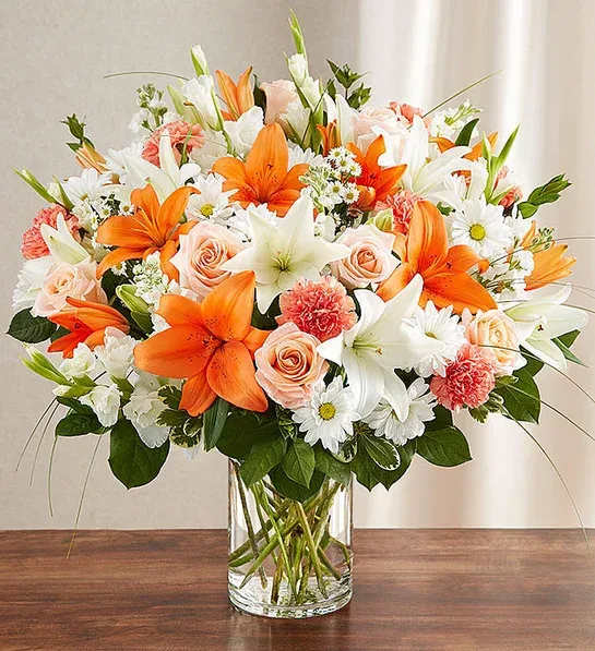 Orange lilies and peach roses in a clear glass vase