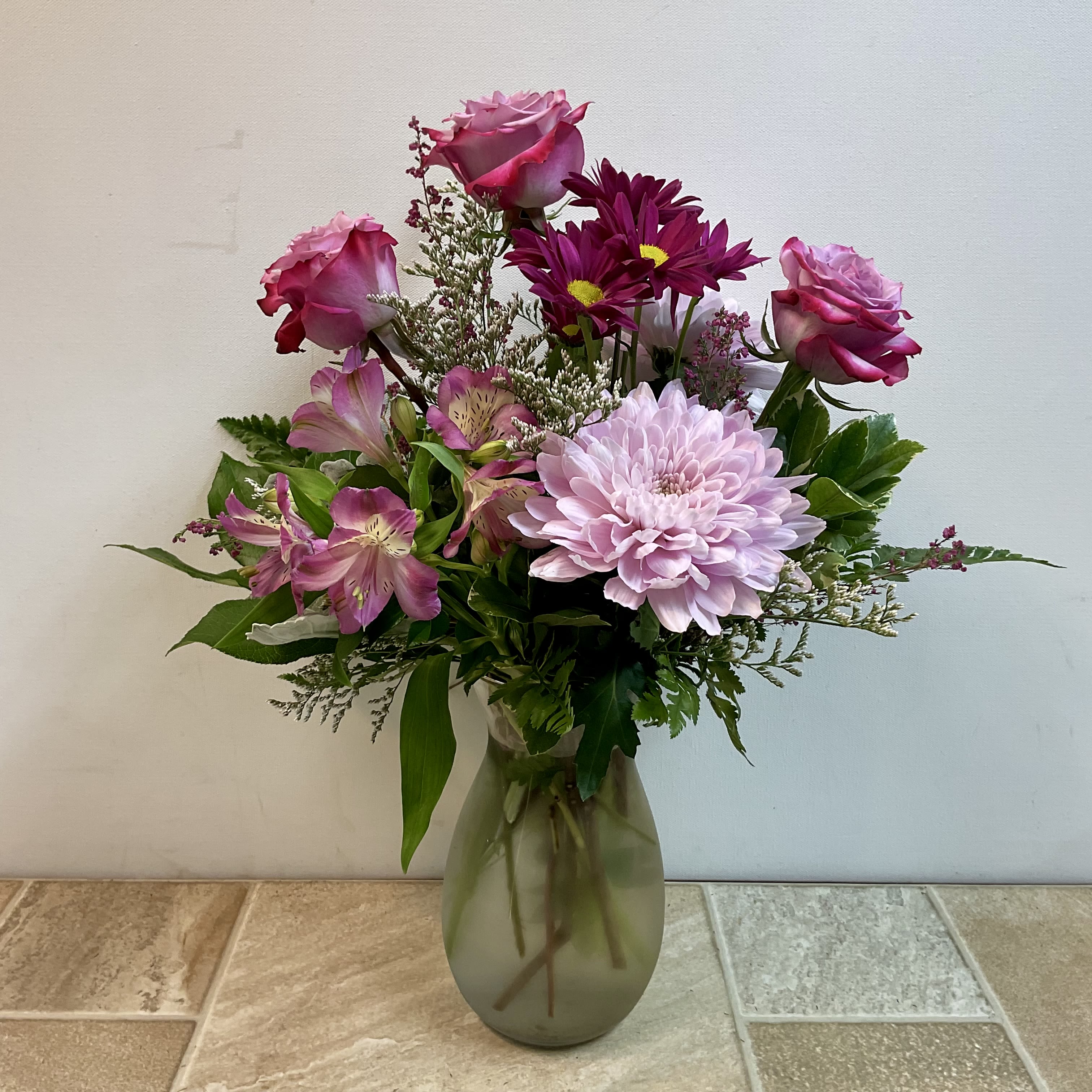 Lavender Lady - A very pretty bouquet of fresh lavender roses, cremone flower, alstroemeria and cushion mums. It’s expertly arranged in a clear glass vase and measures 15” wide x 19” tall.  Primary flowers: rose, mum, lily