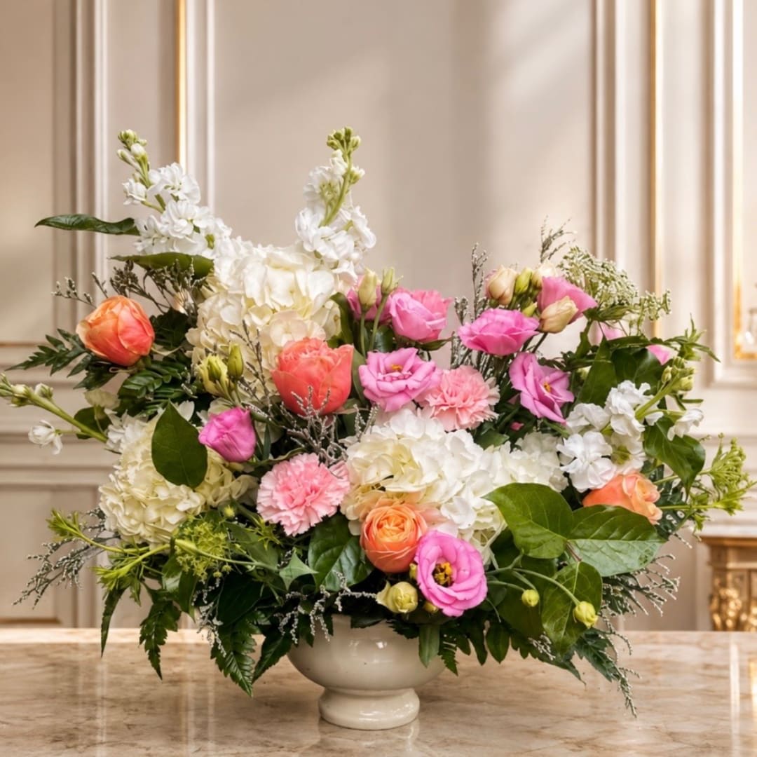 Mixed pink, white, and peach flowers arranged in a white pedestal vase