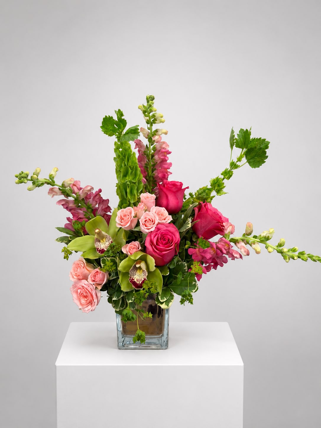 Pink roses and snapdragons arranged in a square glass vase
