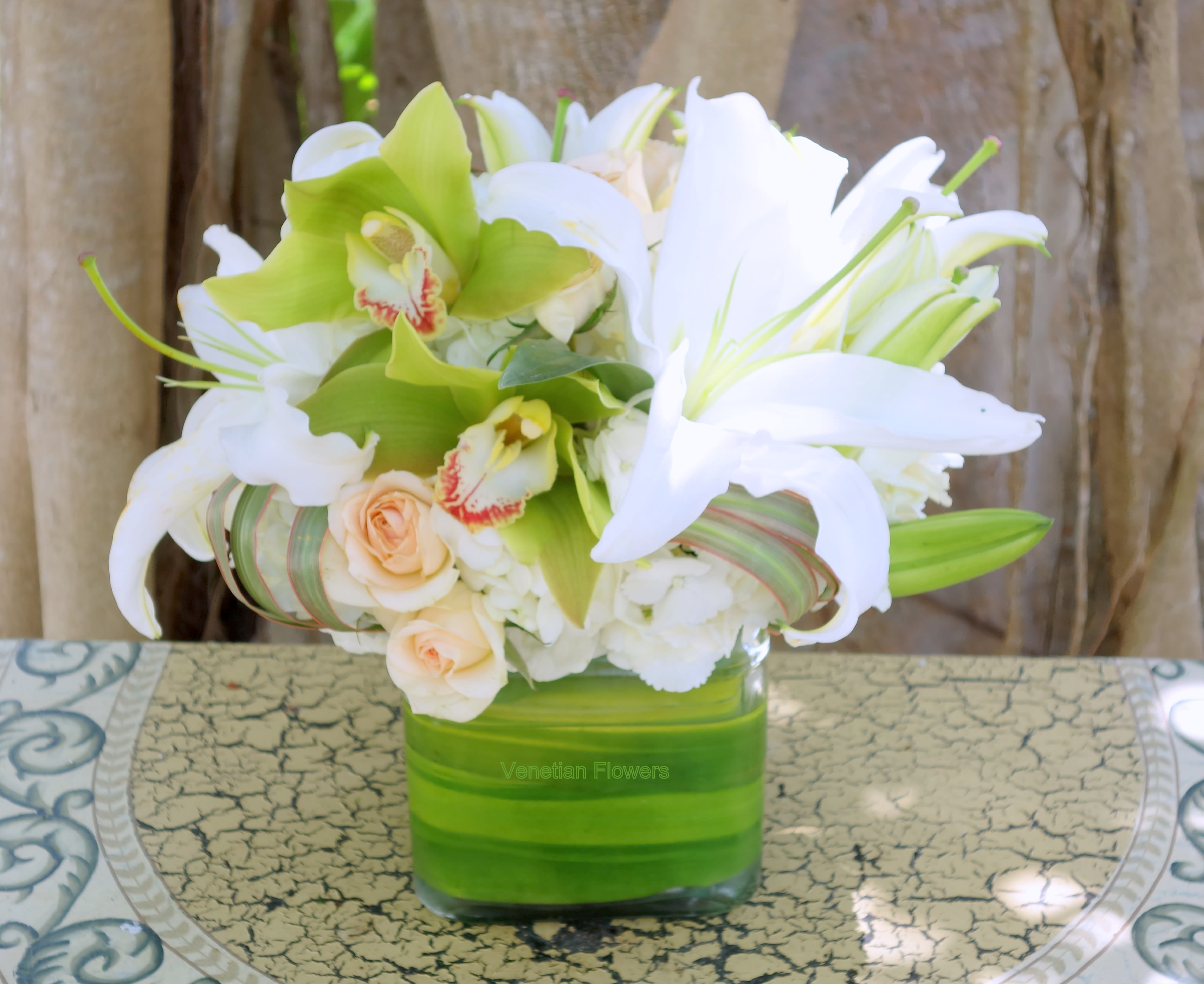 Low arrangement of white lilies, green orchids, and peach roses in a square glass vase