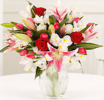Bouquet of pink and white lilies with red roses in a clear glass vase