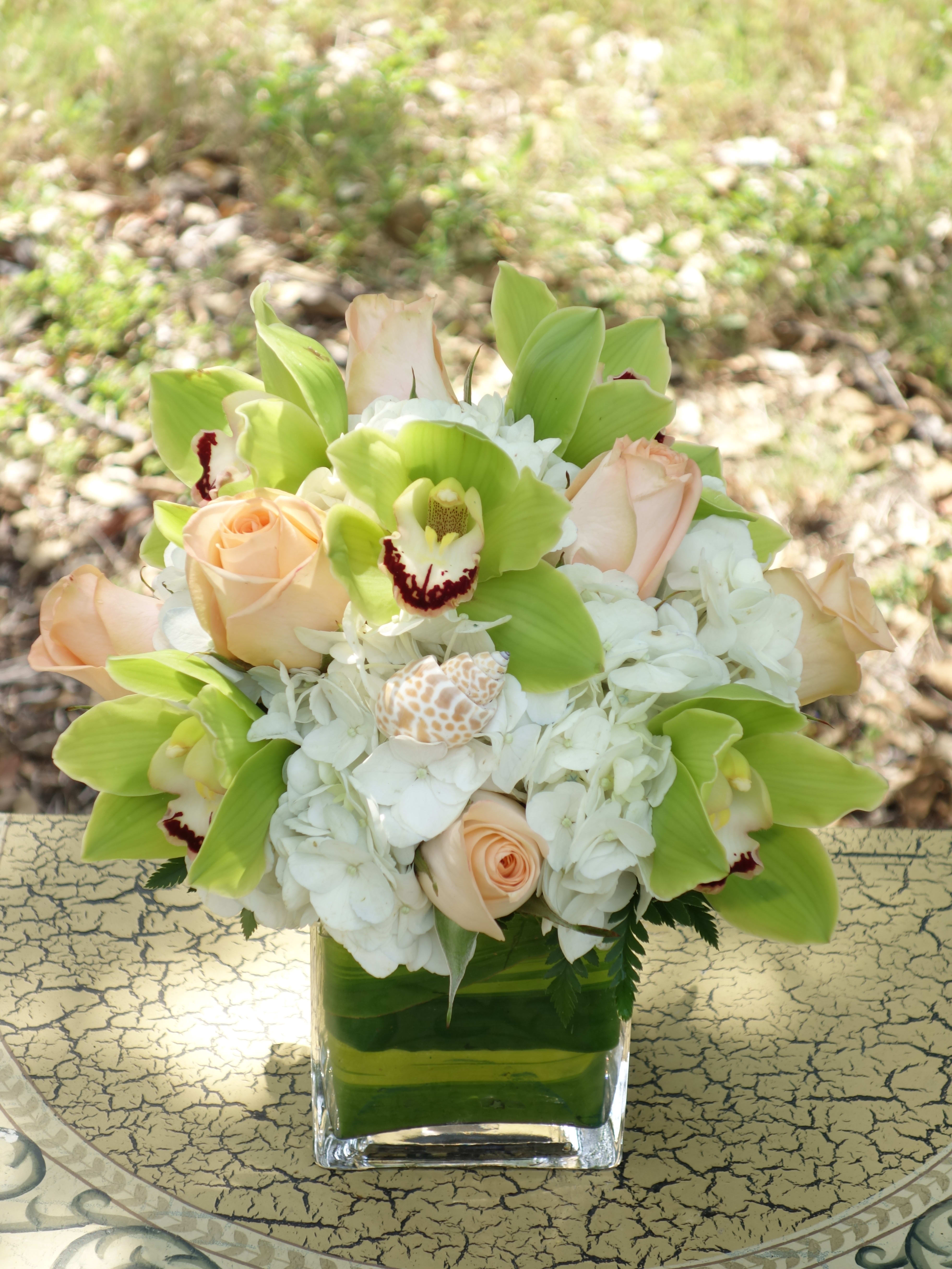 Bouquet of pale roses, white hydrangeas, and green orchids in a square glass vase