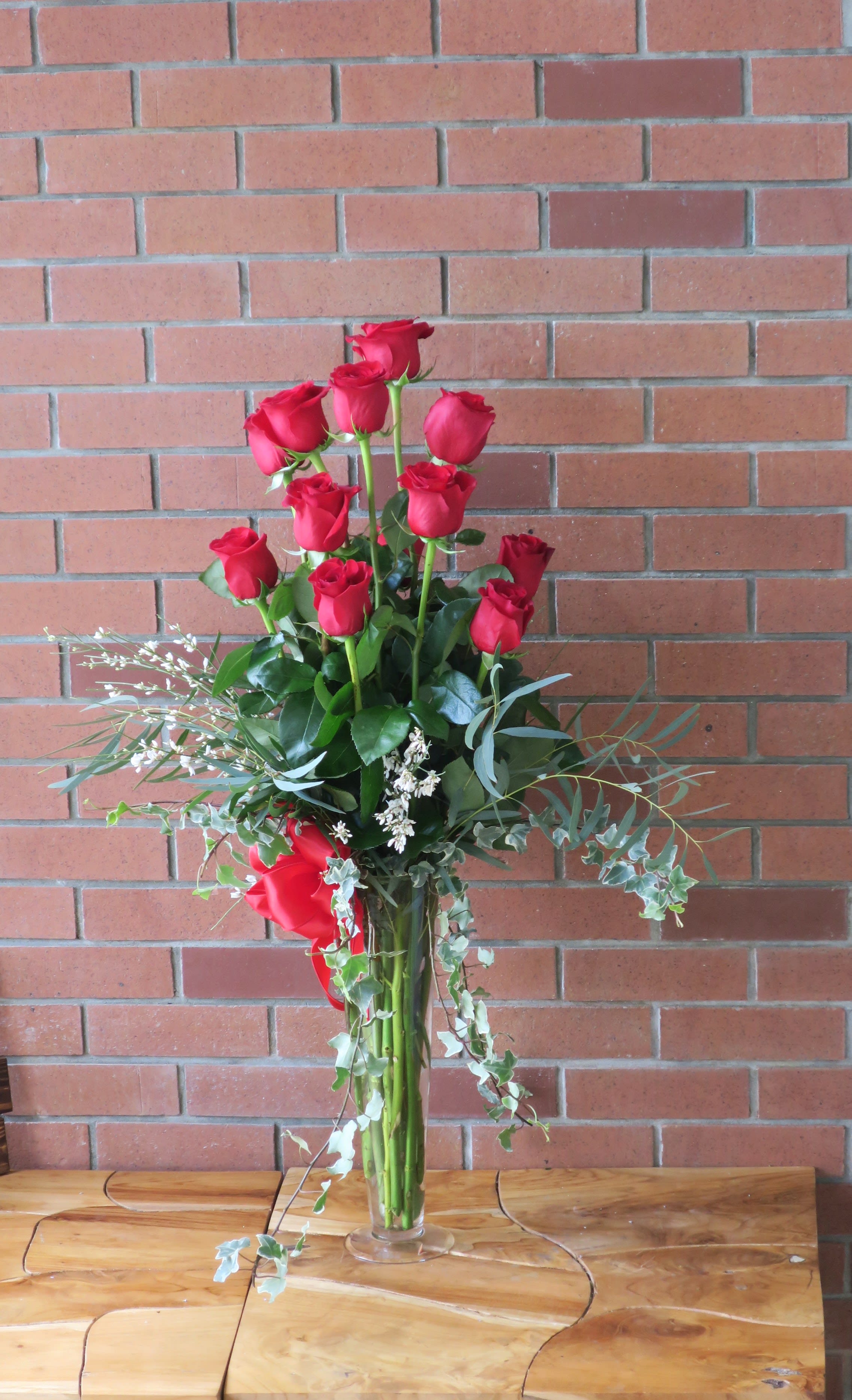 Tall vase arrangement of red roses with trailing greenery