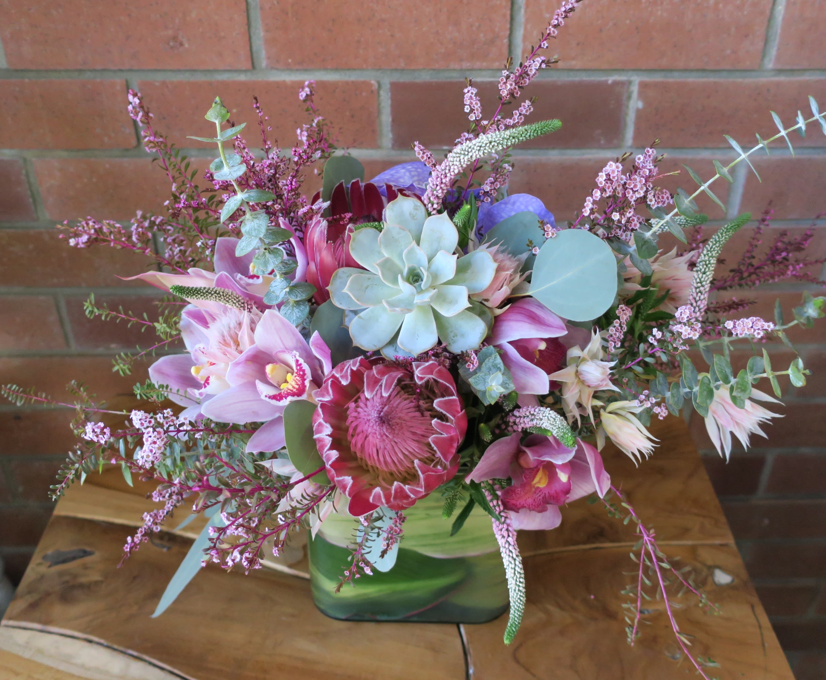 Pink and purple floral arrangement in a green vase with succulents