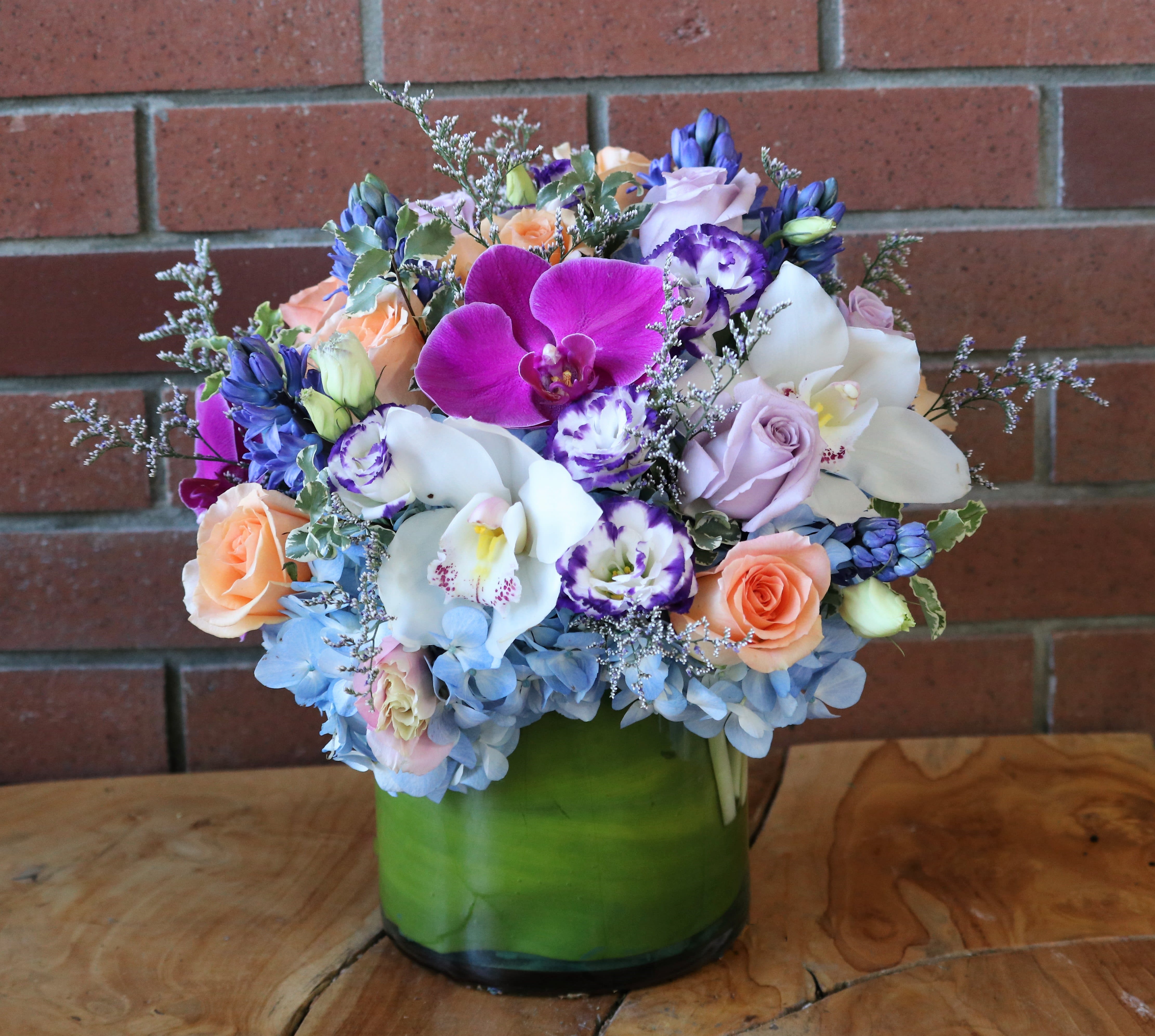 Mixed bouquet of orchids, roses, and hydrangeas in a green glass vase