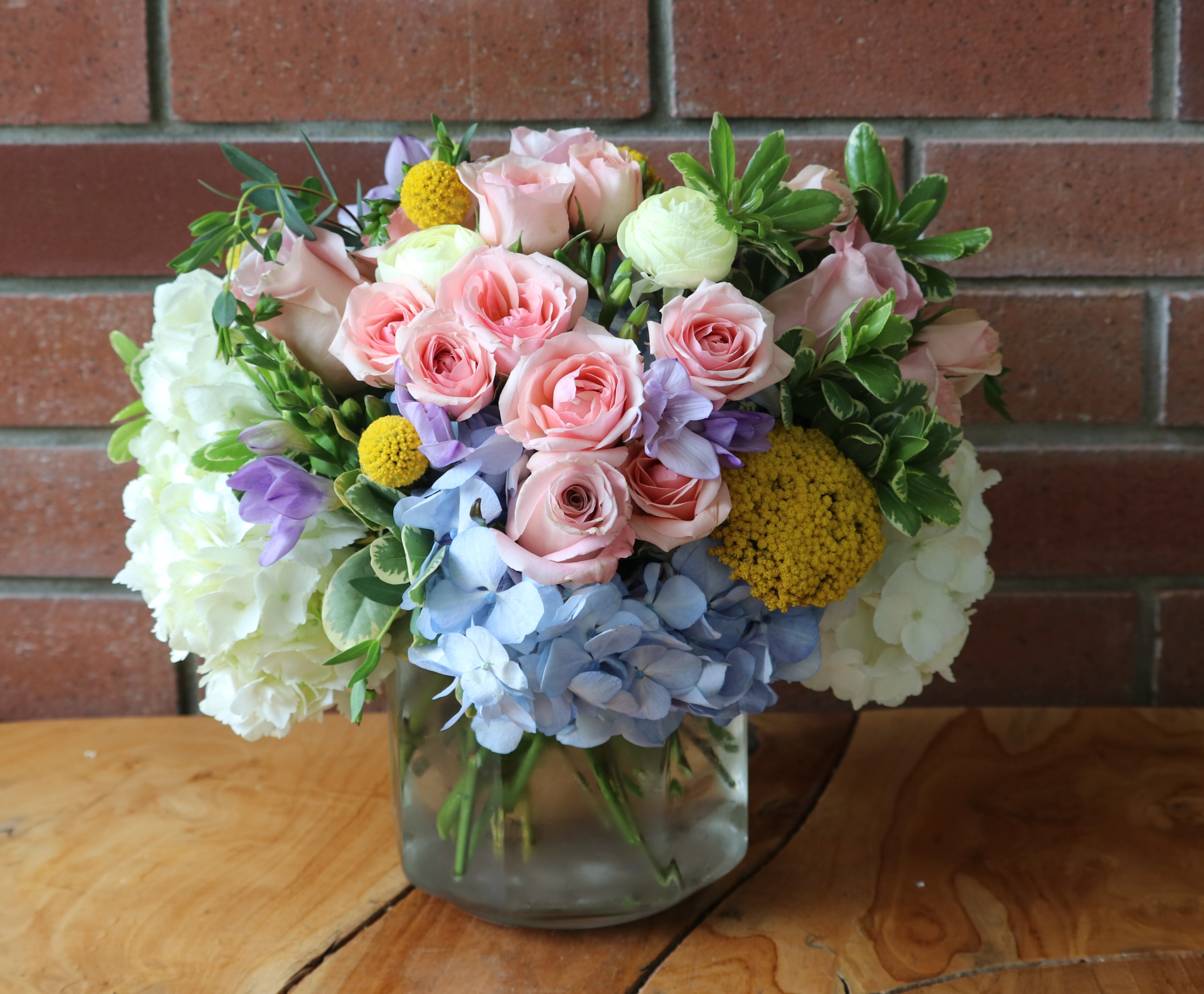 Bouquet of pink roses, hydrangeas, and yellow accents in a glass vase