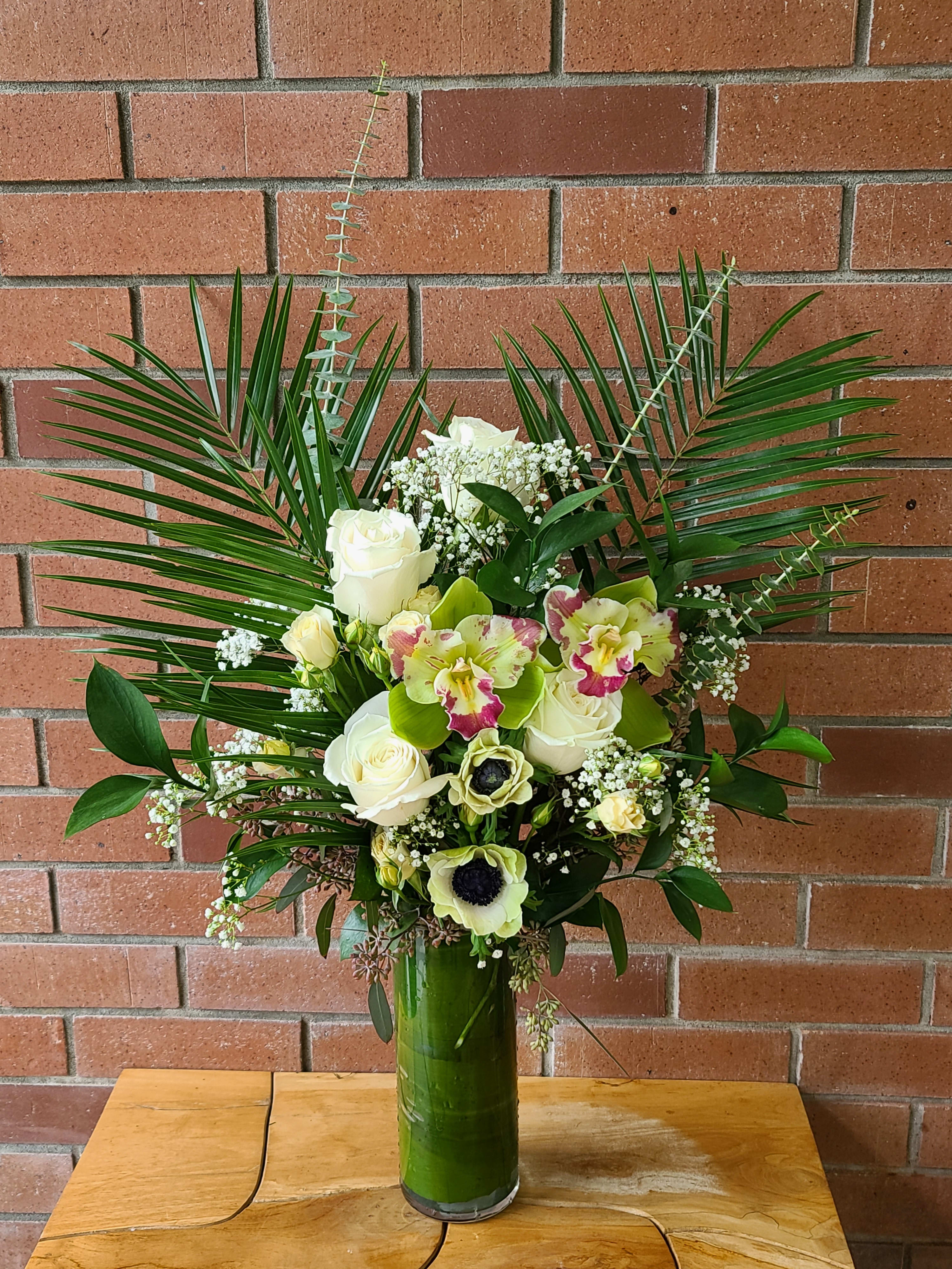 Tall floral arrangement with white roses and orchids in a green vase
