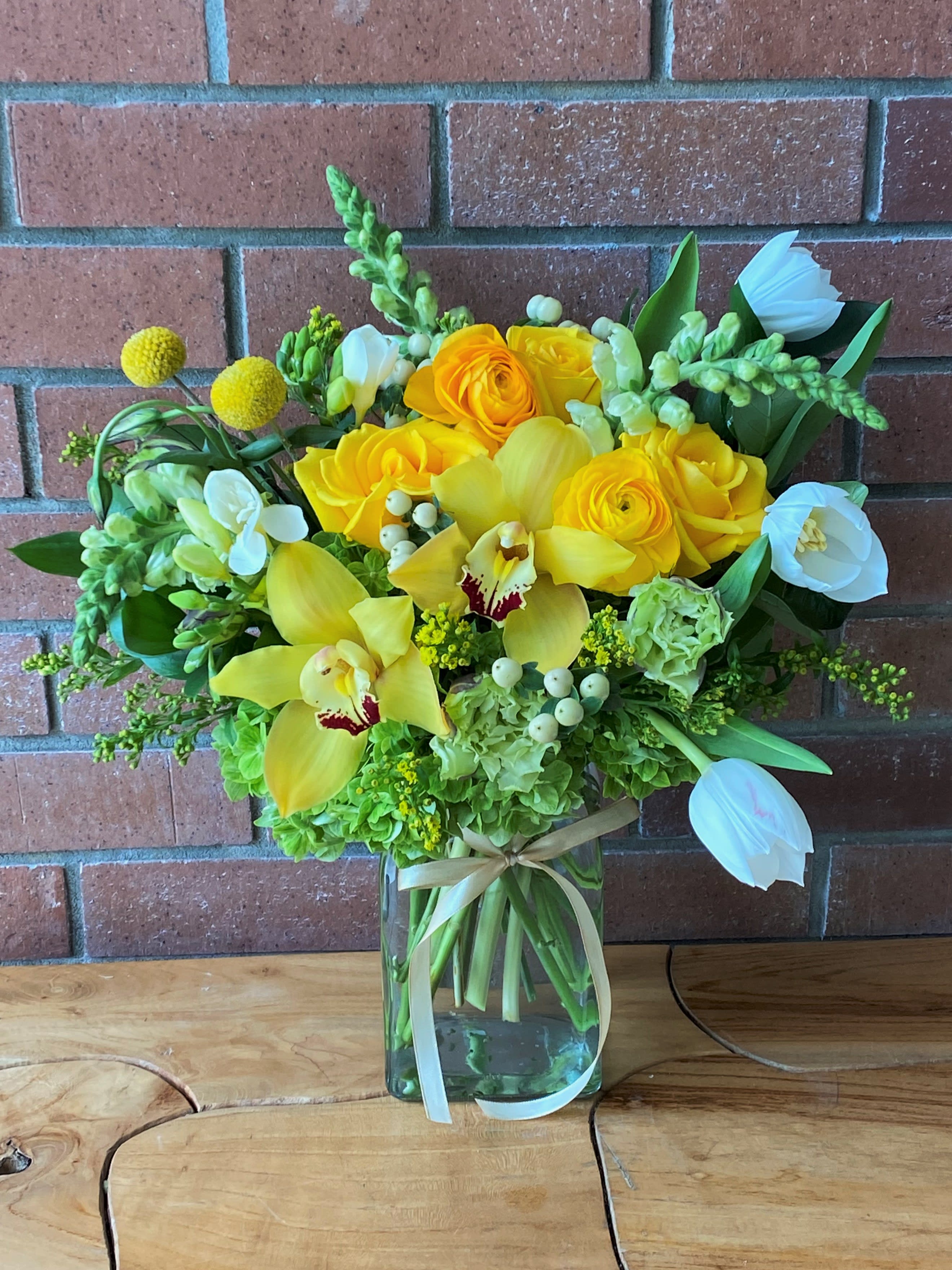 Yellow and white floral arrangement in a glass vase with a ribbon
