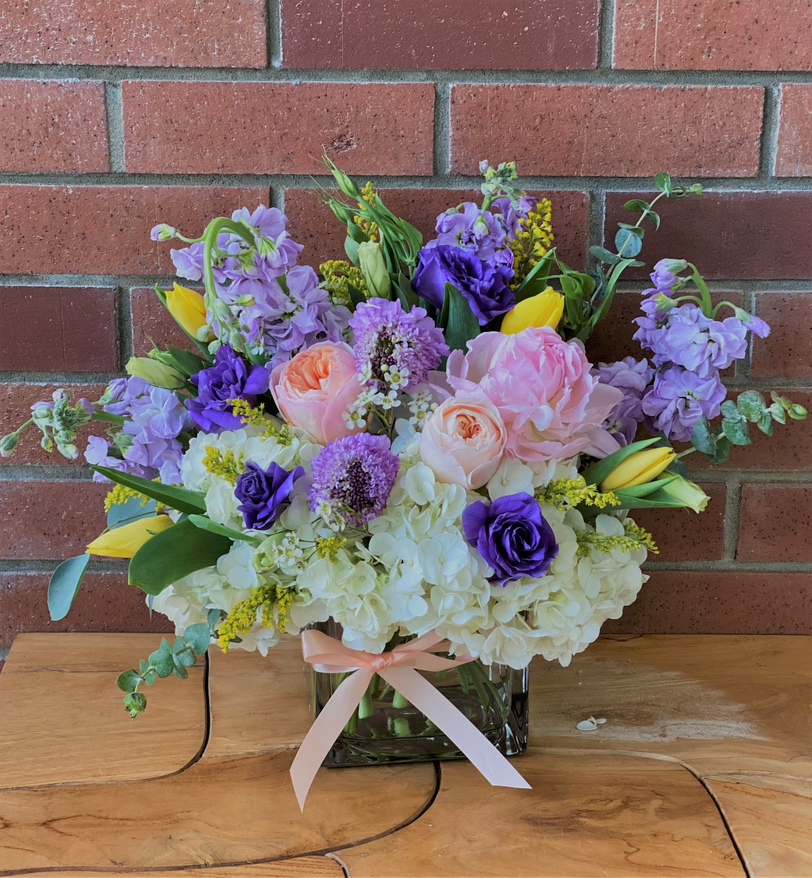 Bouquet of pink, purple, and yellow flowers in a glass vase with a ribbon